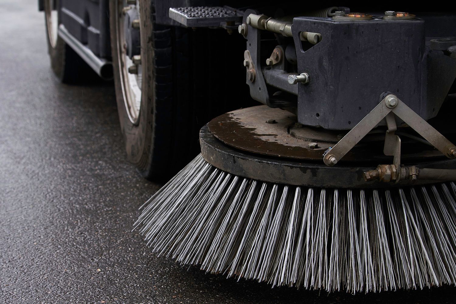 Street sweeper brush sweeping wet asphalt, close-up view.