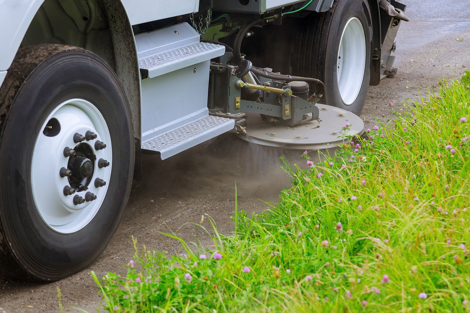 Street sweeper spraying the edge of a road lined with green grass.