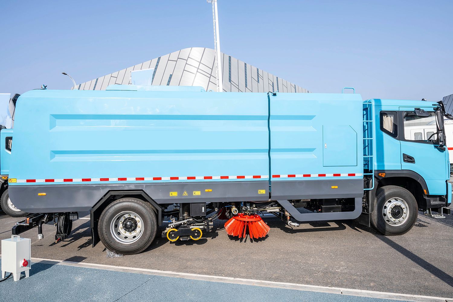 Blue street sweeper truck on pavement, red brush visible.