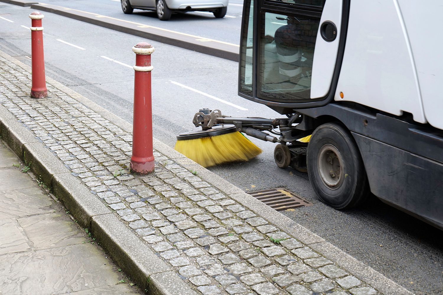Street sweeper cleaning a road, dust and debris visible.