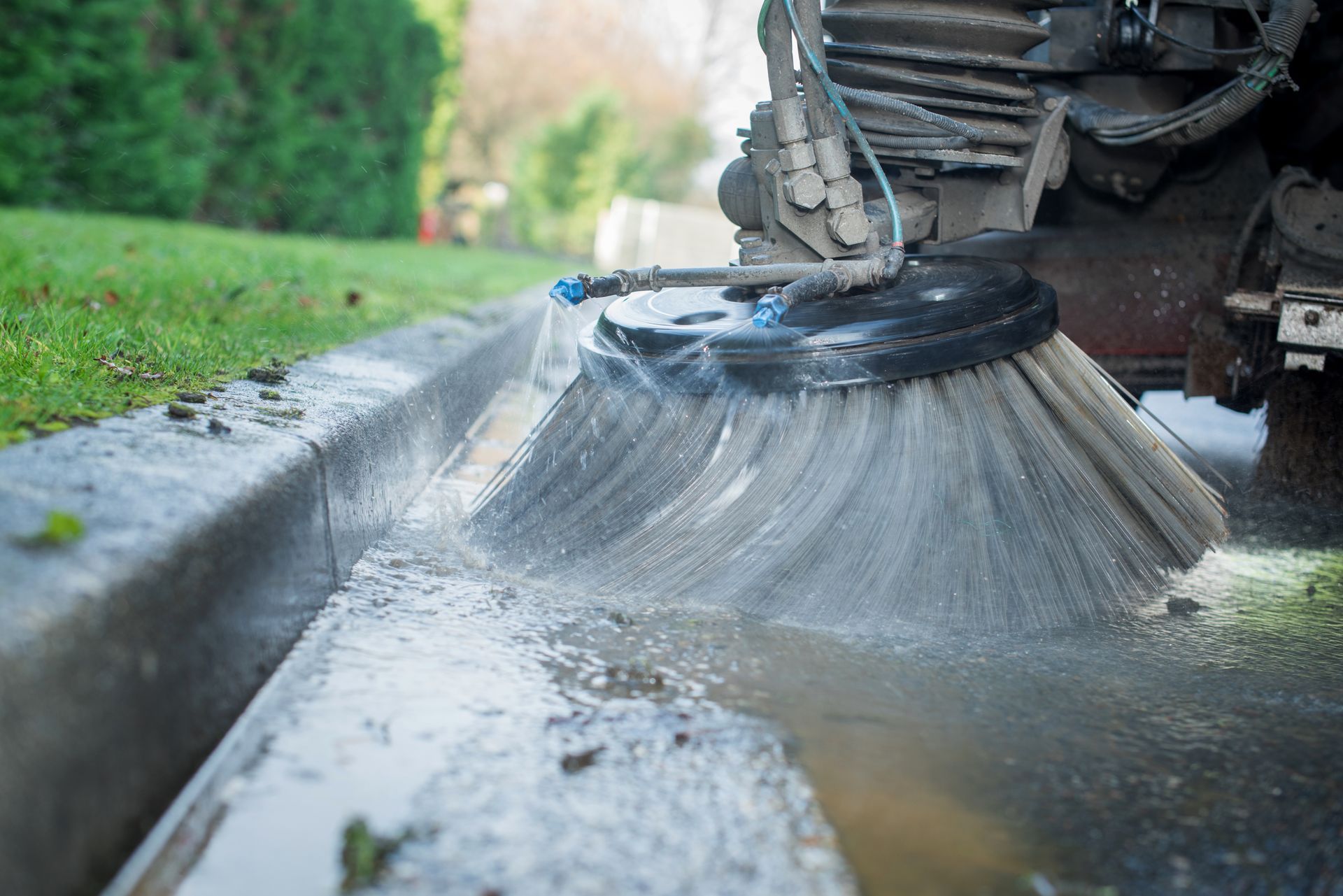 Sweeper brush spraying water along a curb