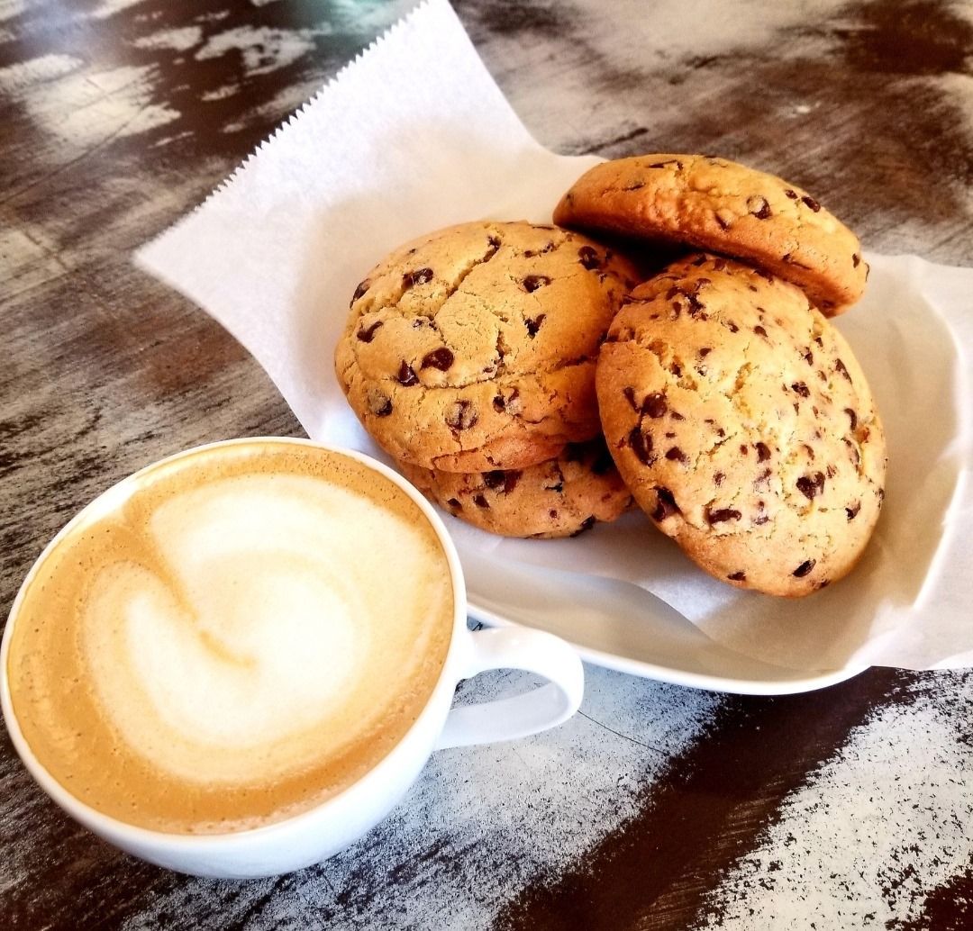 A bowl of chocolate chip cookies next to a cup of cappuccino
