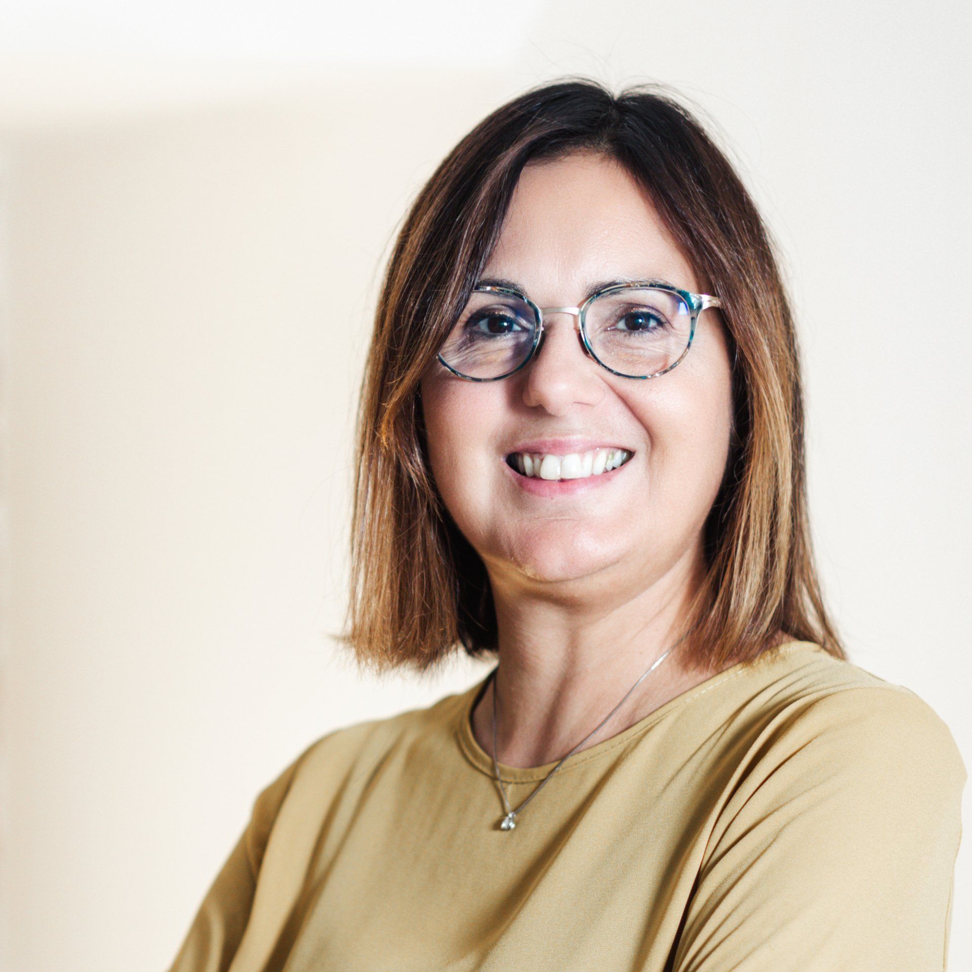 Una donna che indossa occhiali e una collana sorride alla macchina fotografica