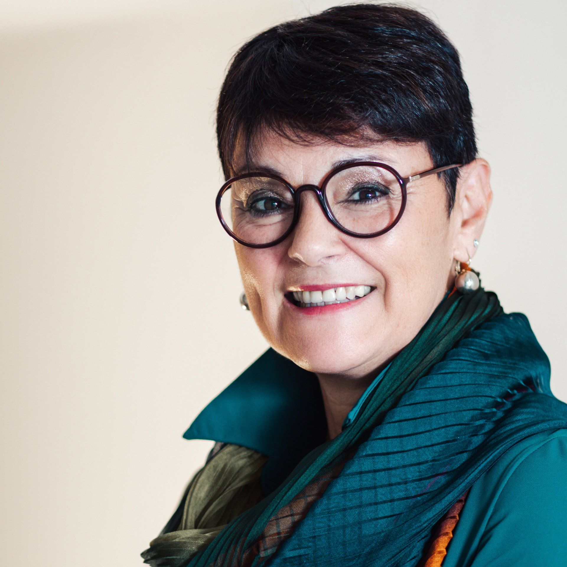 Una donna che indossa gli occhiali e una sciarpa verde sorride alla telecamera