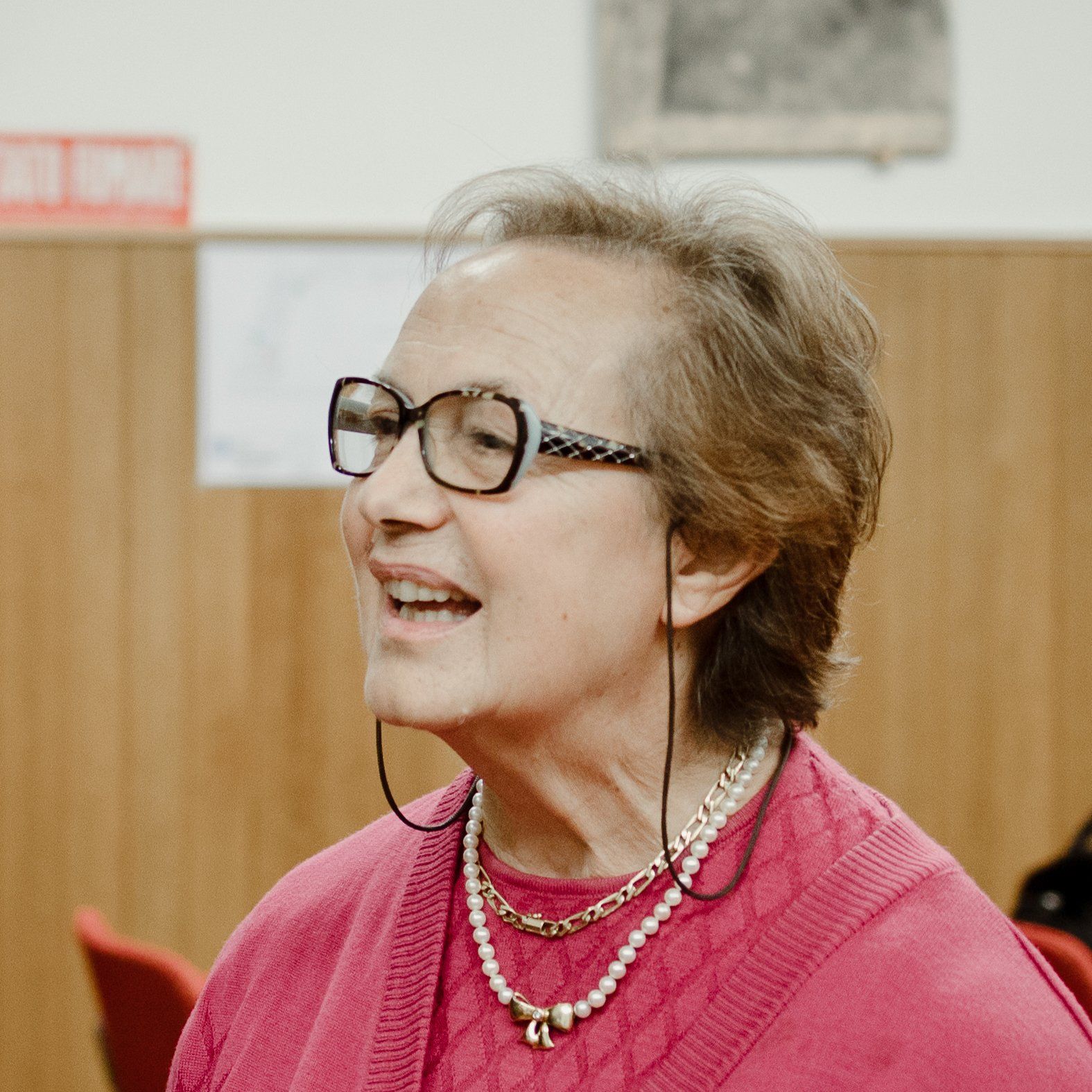 Una donna che indossa occhiali e una collana di perle sorride.
