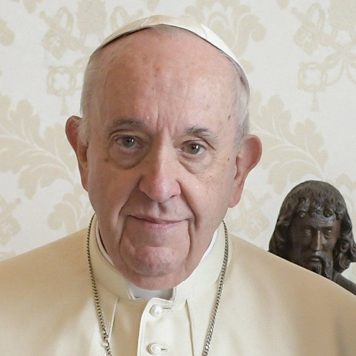 Un uomo vestito di bianco è in piedi accanto a una statua di Gesù