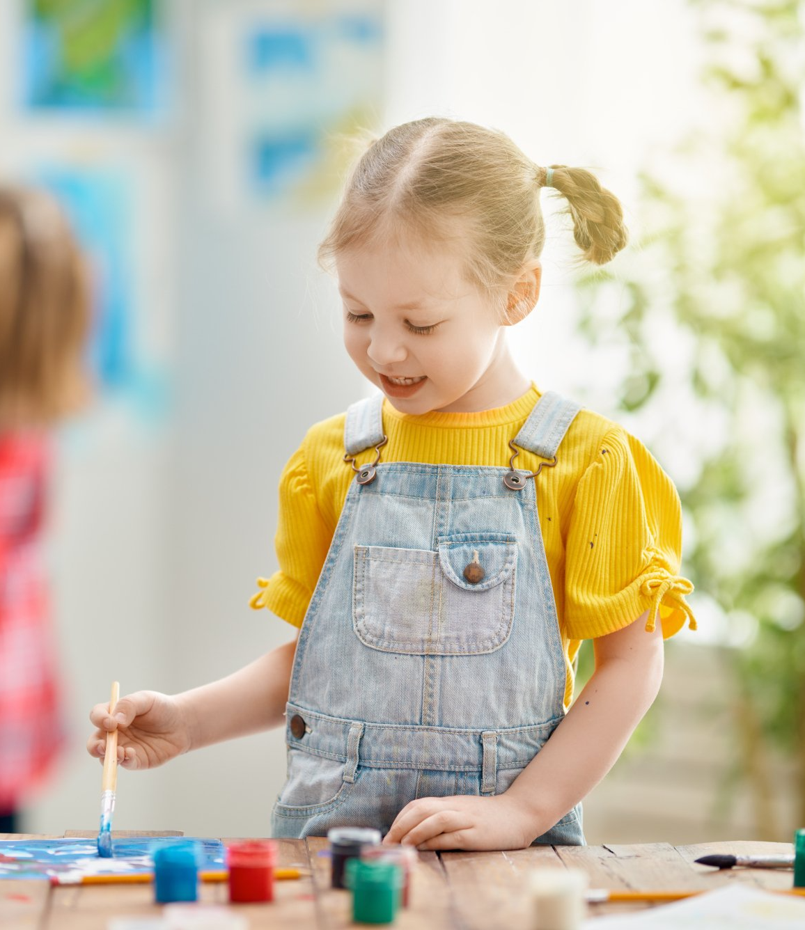Una bambina è seduta al tavolo e dipinge con un pennello.