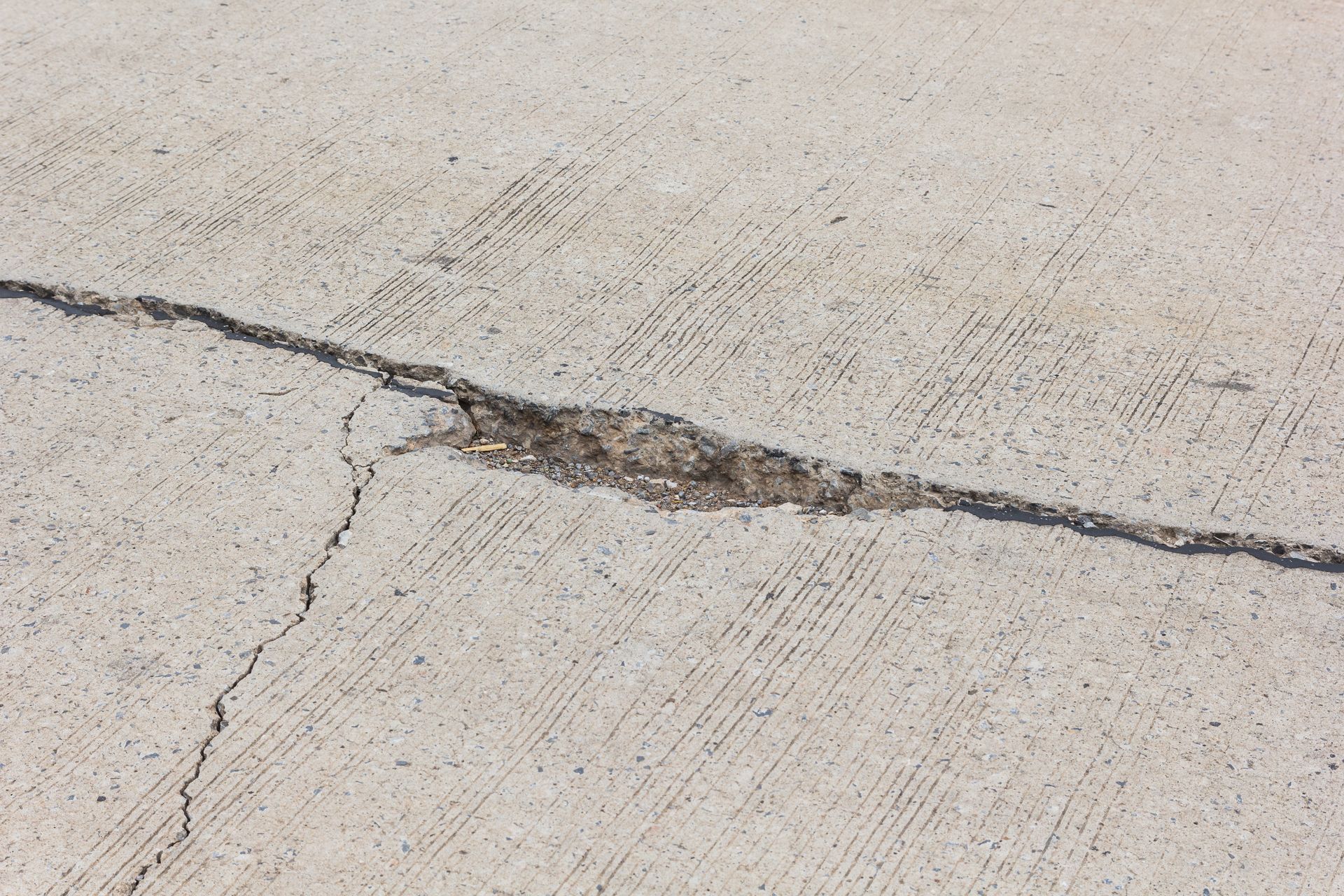 Cracked concrete pavement with a long dark fissure running across the surface