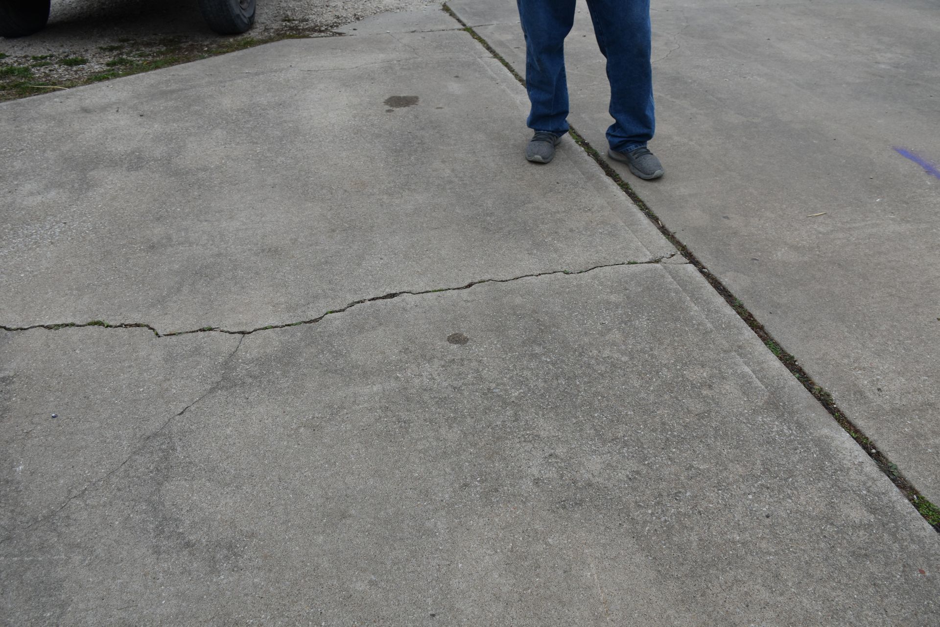 Cracked concrete sidewalk with a person’s legs and feet visible near the top edge.