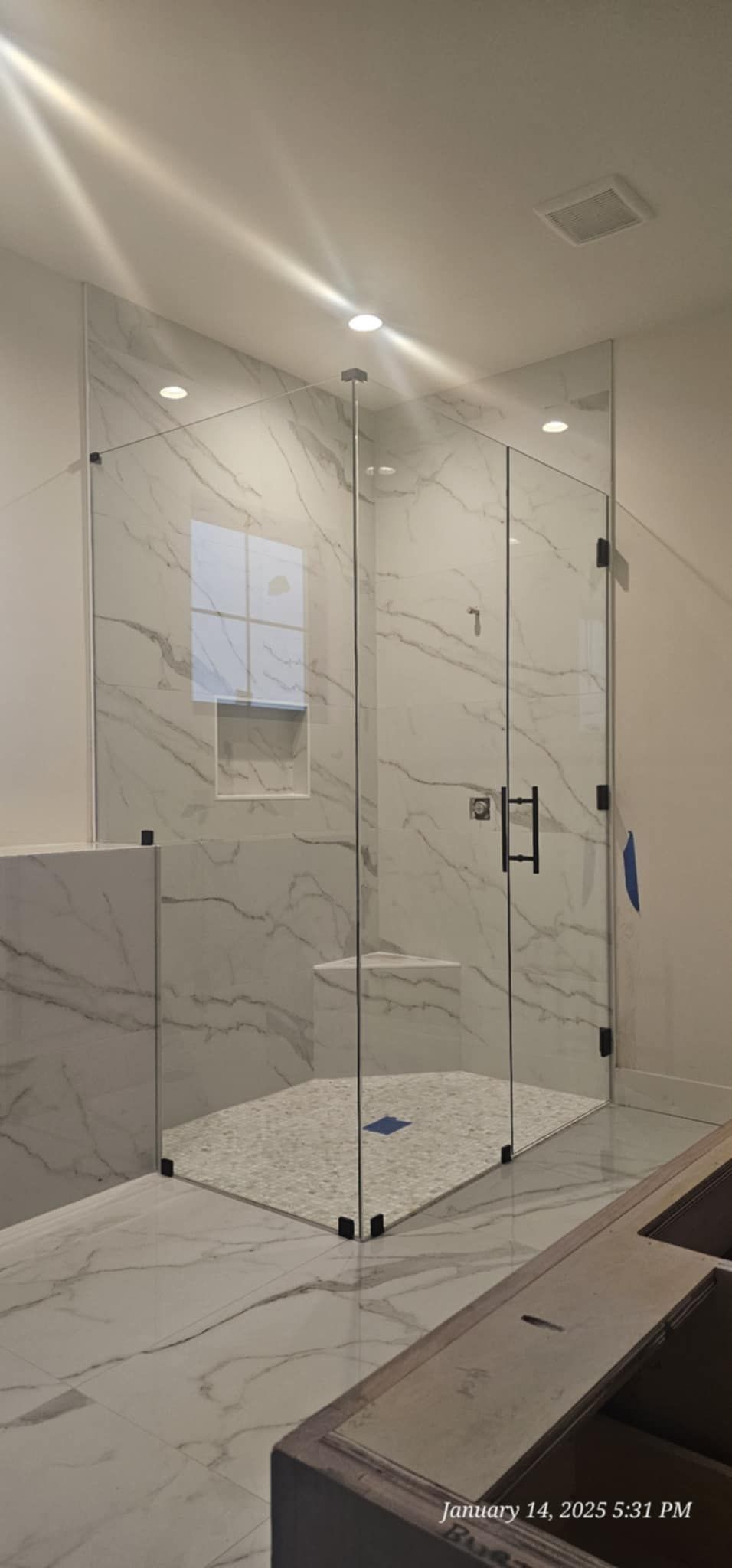 A newly installed frameless glass shower enclosure with marble tile in a modern bathroom.