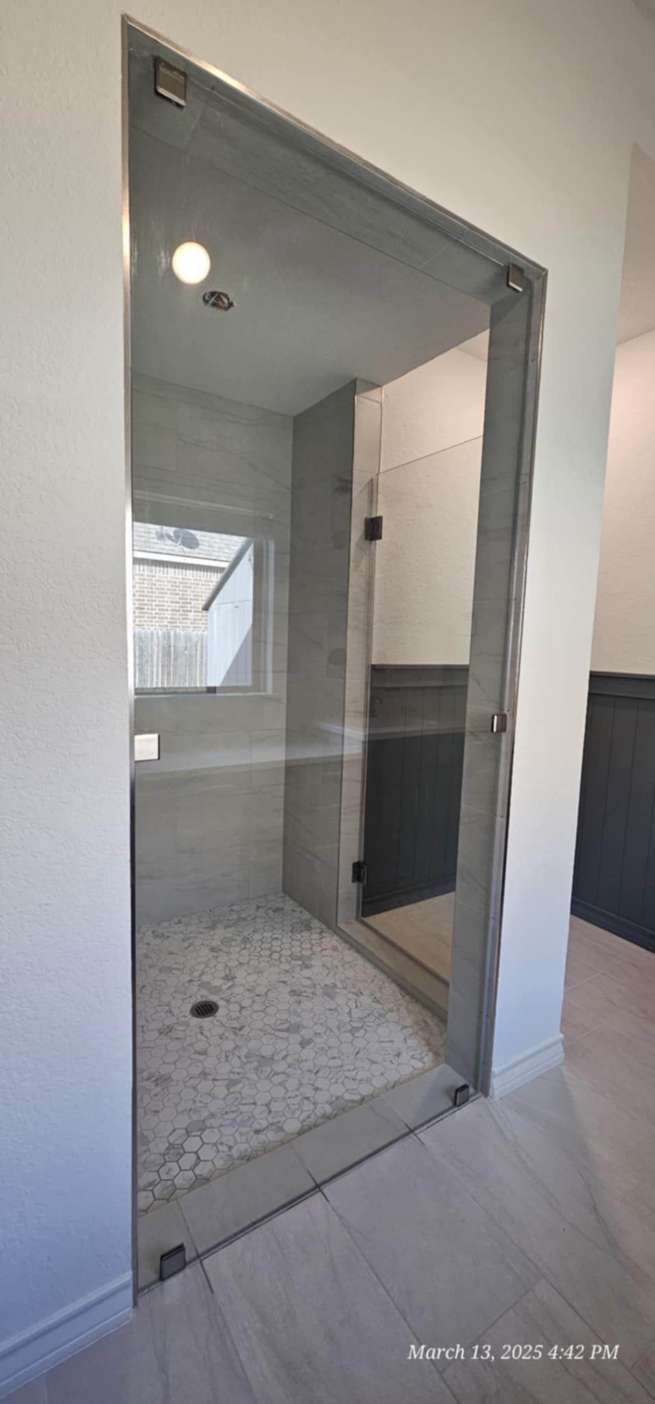 A glass shower enclosure with pebble flooring, and white walls, in a modern bathroom.