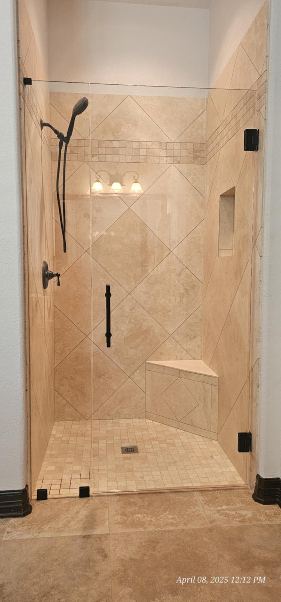 Shower stall with glass doors, brown tile, and black fixtures.