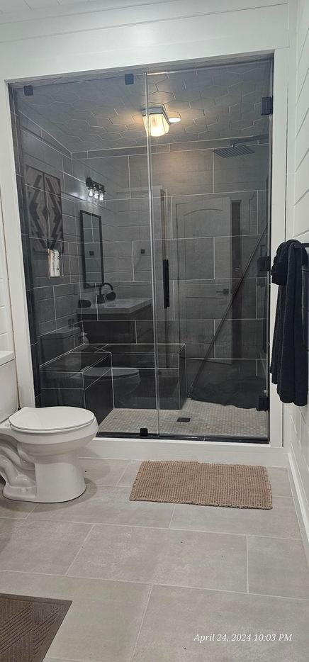 Bathroom with gray tile, glass shower, toilet, and bath mat.