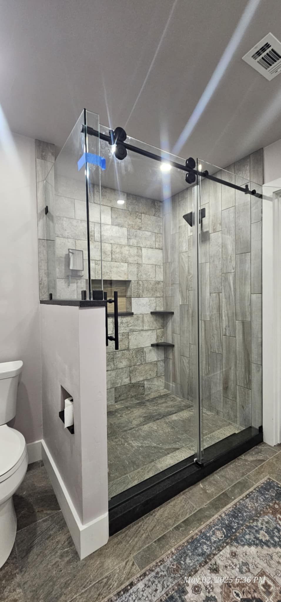 Modern bathroom with a glass shower door and textured stone wall.
