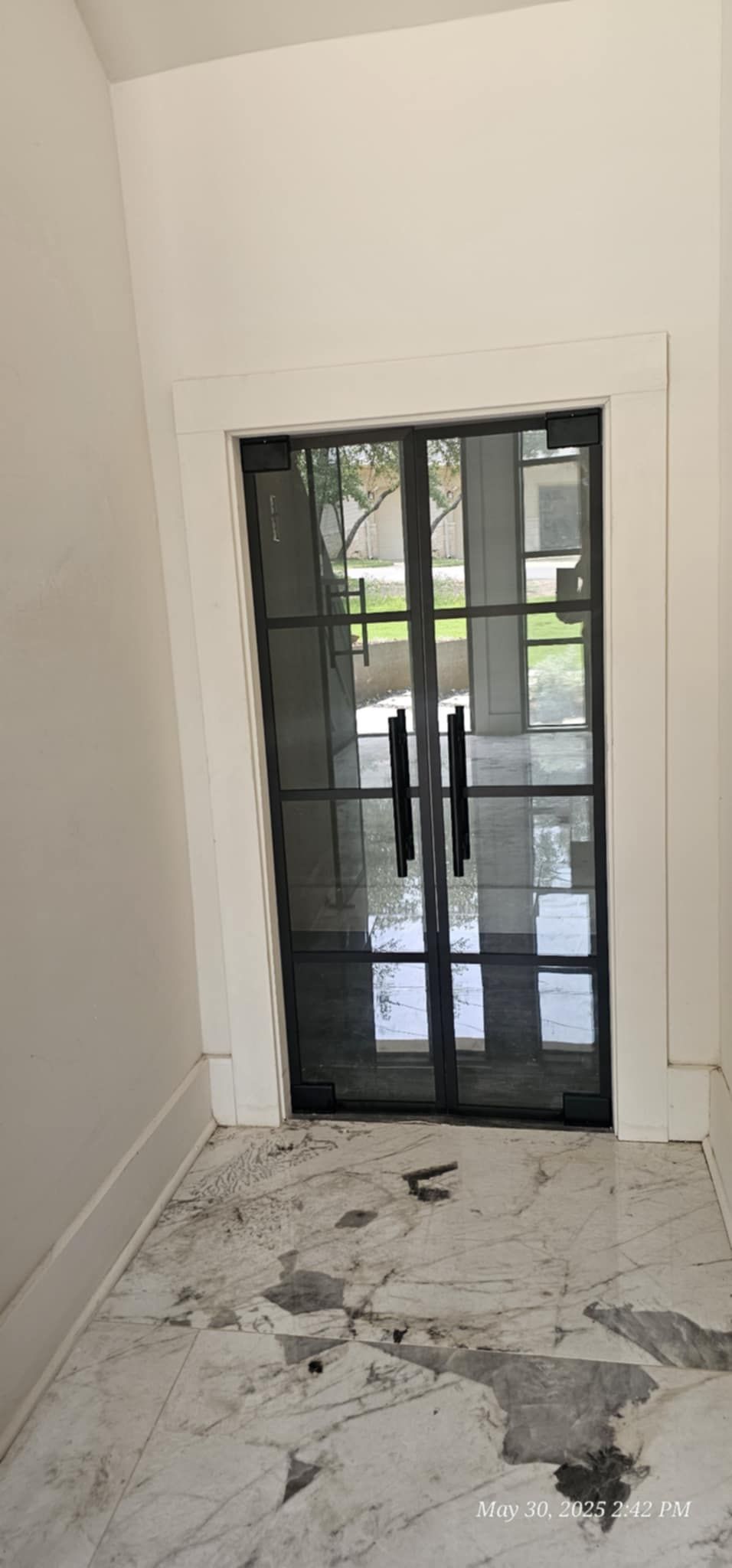 Glass double doors with black metal framing and handles. White walls and marble tile floor.
