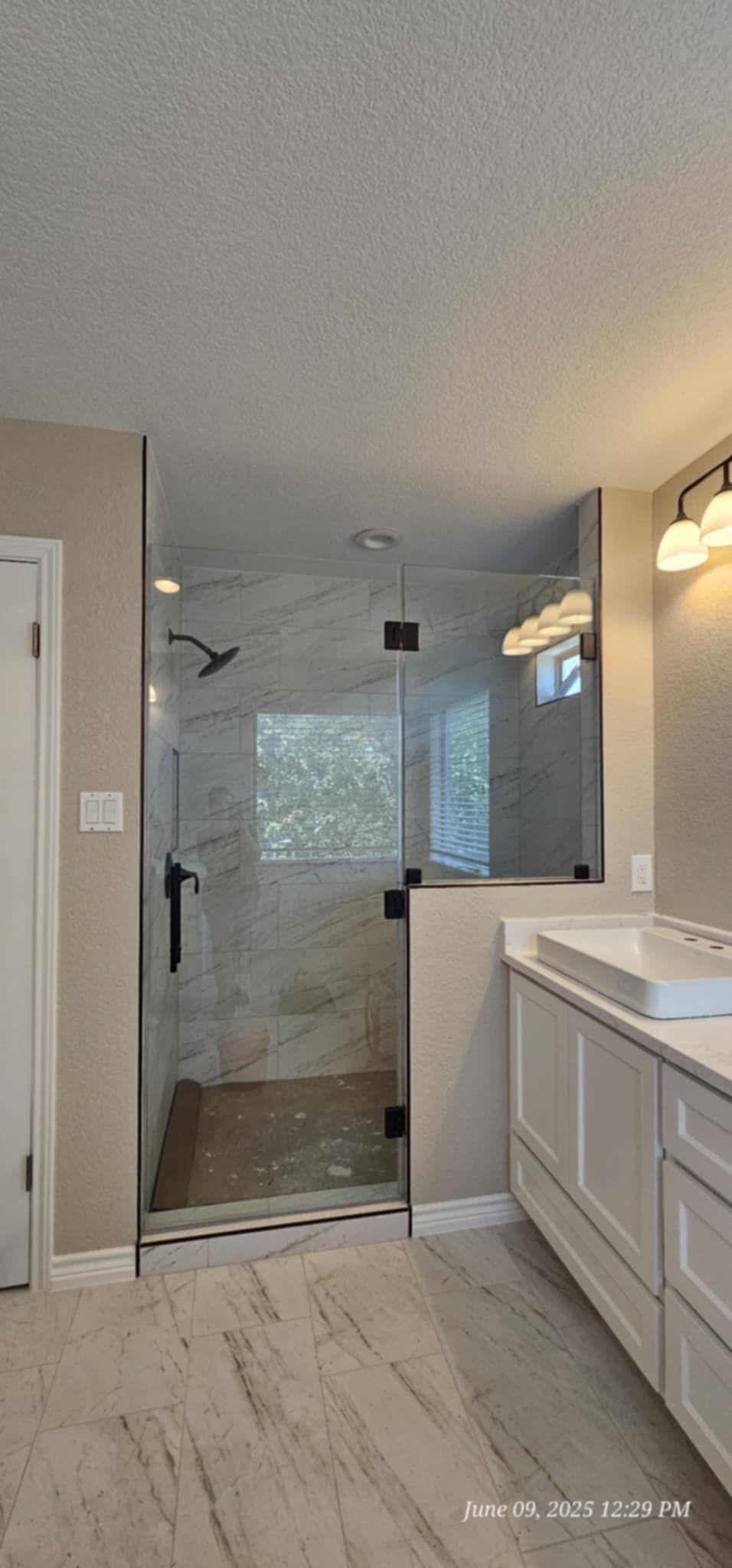 Bathroom with glass shower, white vanity, and marble-like floor. The shower has black hardware.
