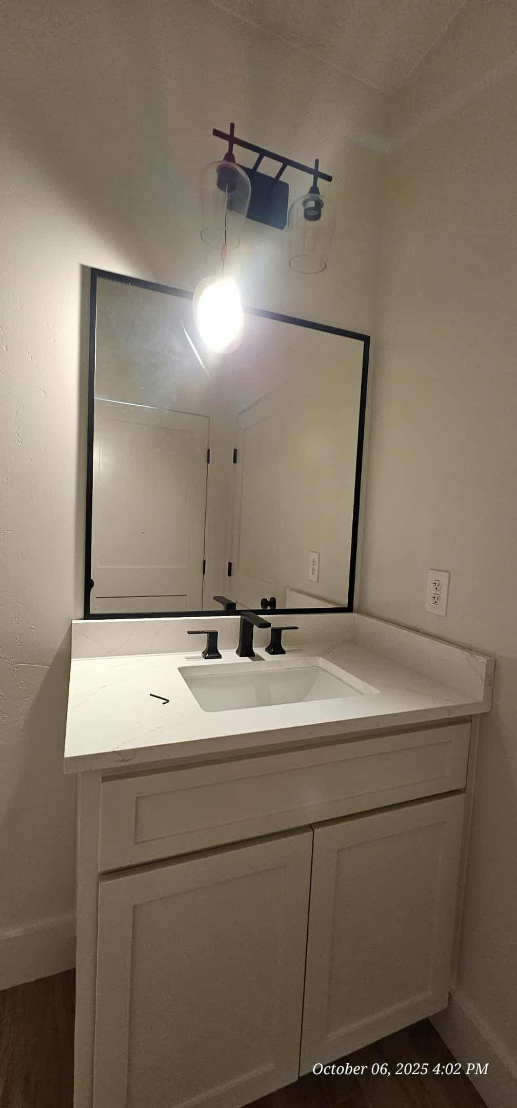 Bathroom vanity with white countertop, black fixtures, and a mirror with a black frame. White cabinet with two doors.