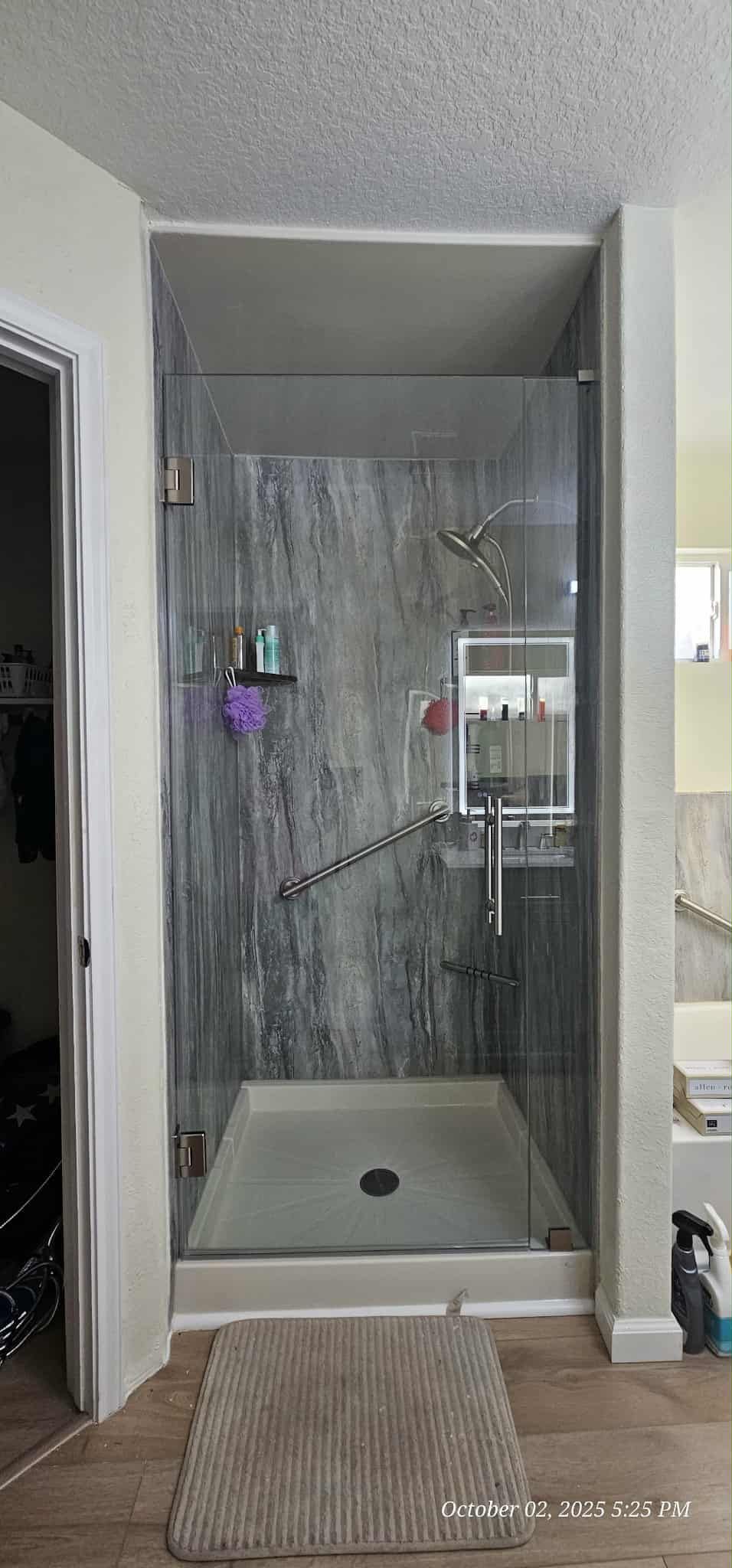 A walk-in shower with gray walls and glass doors. A woven rug sits on the floor outside the shower.