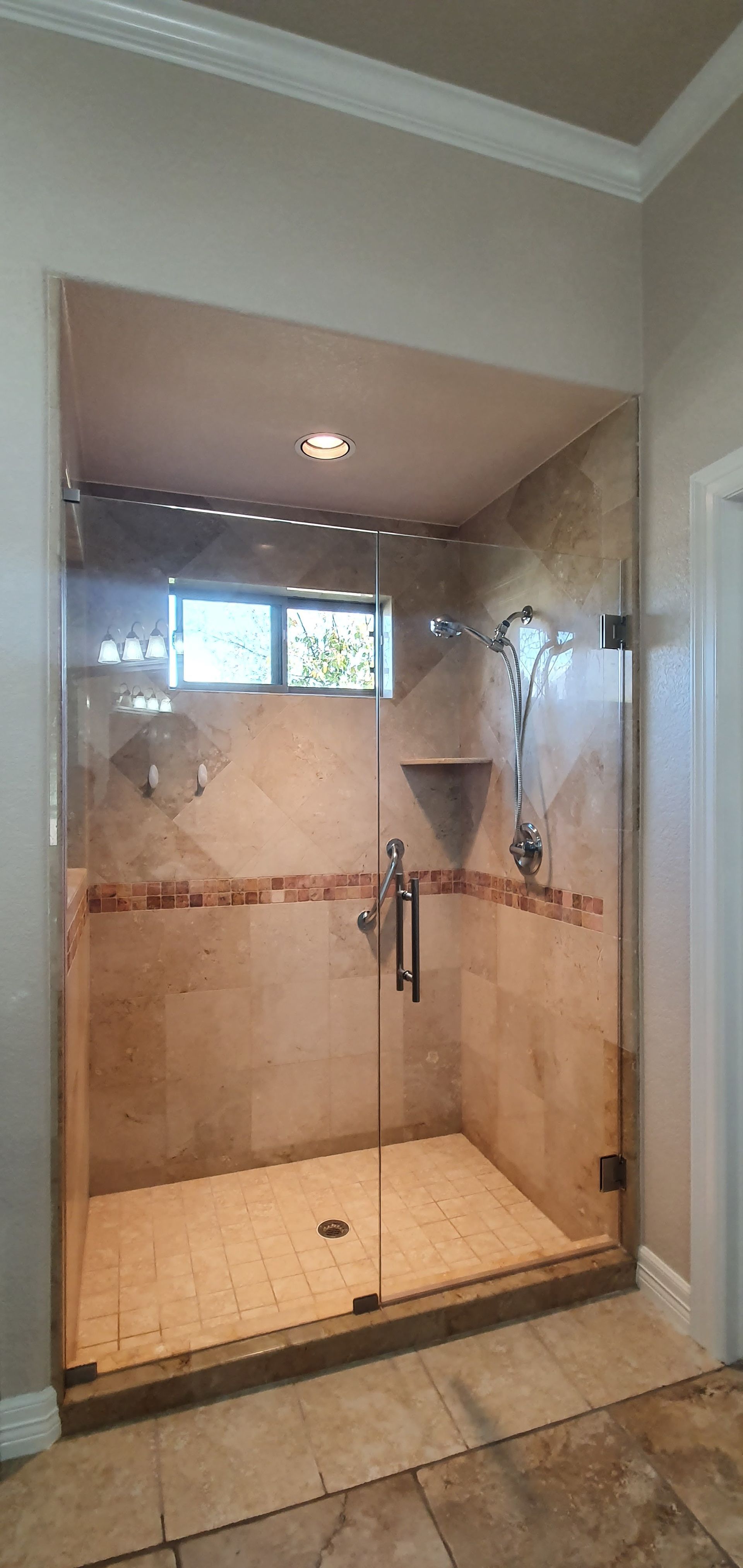 Glass-enclosed shower with beige tile walls and floor. Chrome fixtures, including a shower head and handles.