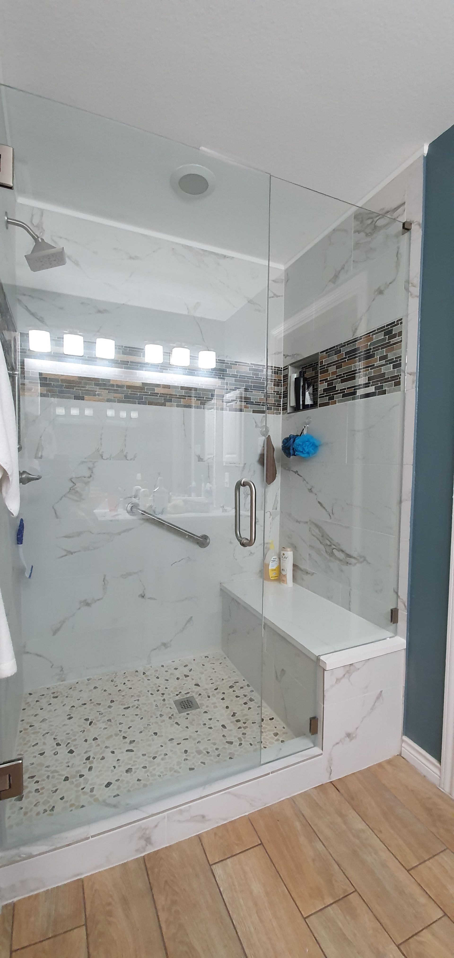 A modern shower with marble-like tile, a glass door, a built-in bench, and a pebbled shower floor.