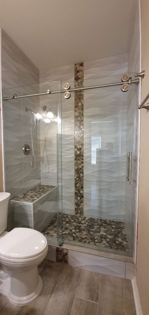 Bathroom with glass shower, stone floor and bench. Silver sliding door hardware. White toilet.