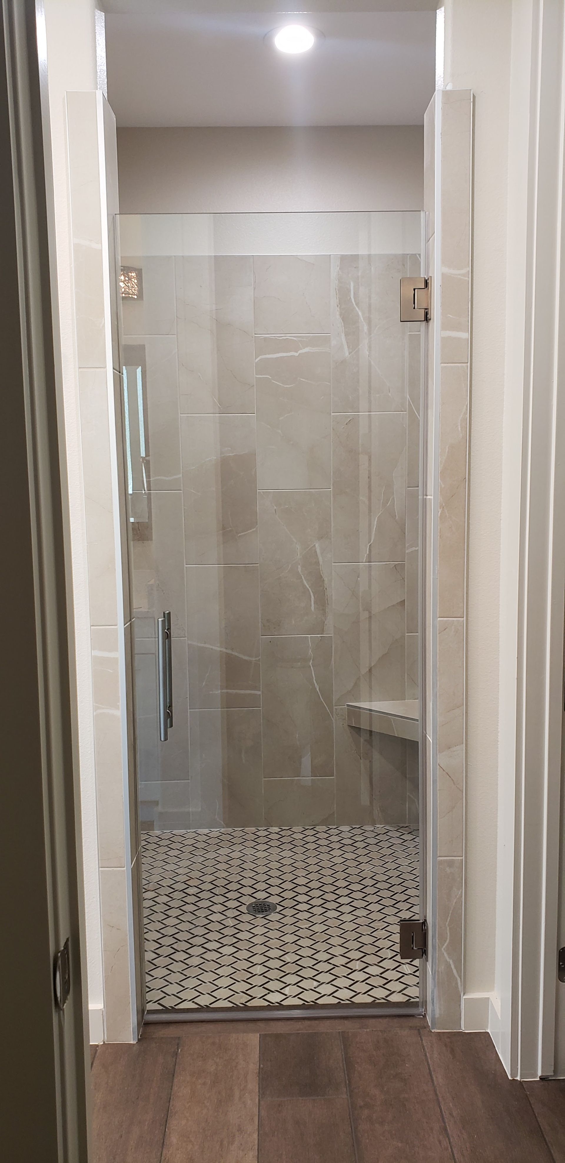 Walk-in shower with glass door and pebble tile floor. Brown tile walls and white trim.