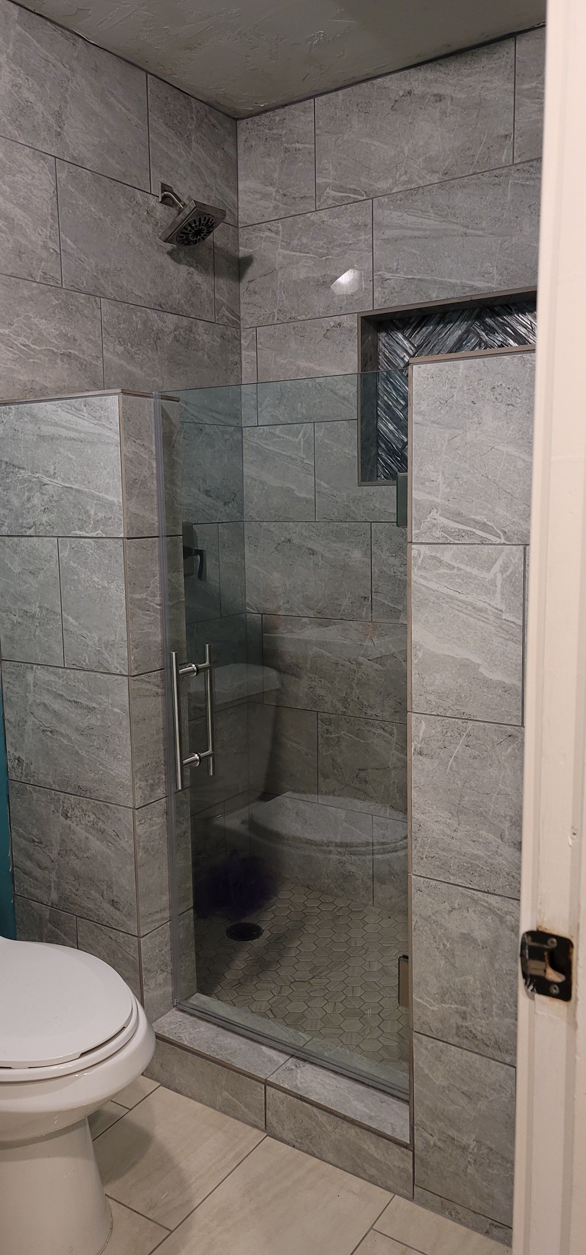 A modern bathroom with a glass shower, toilet, and gray stone tile walls.