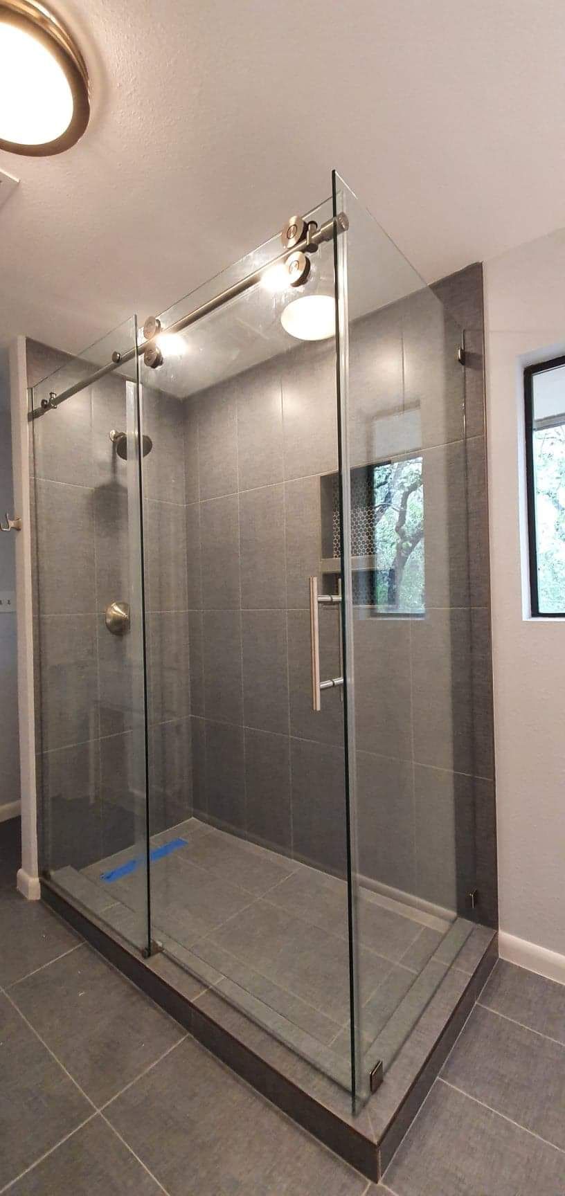 A modern bathroom shower with glass doors, gray tiles, and chrome fixtures.