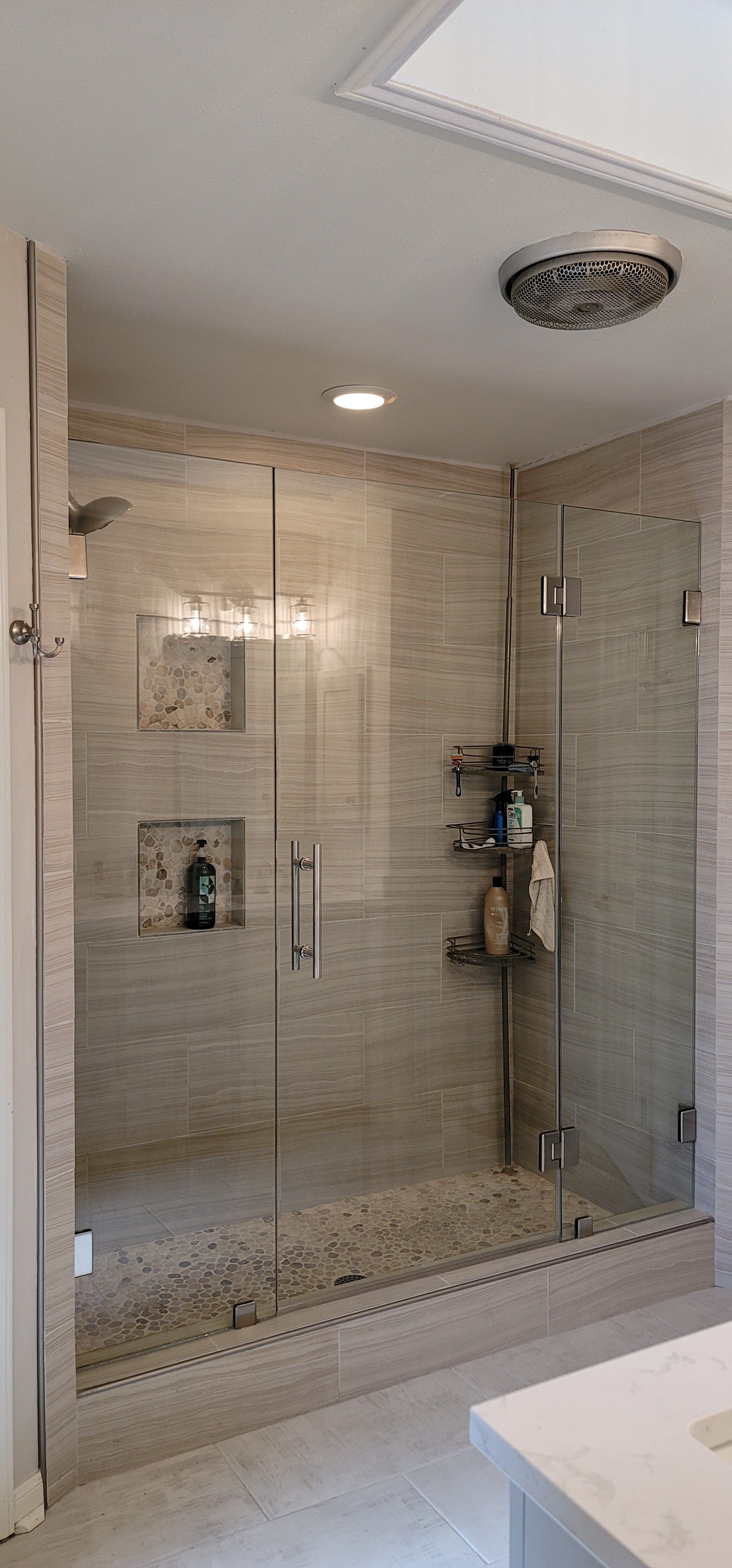 A modern shower with clear glass doors and stone tile walls.