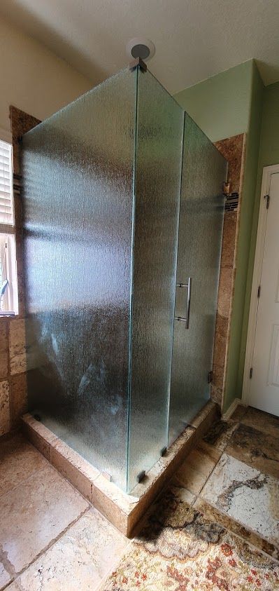 A textured glass shower enclosure with a wooden base, set in a bathroom with stone flooring.