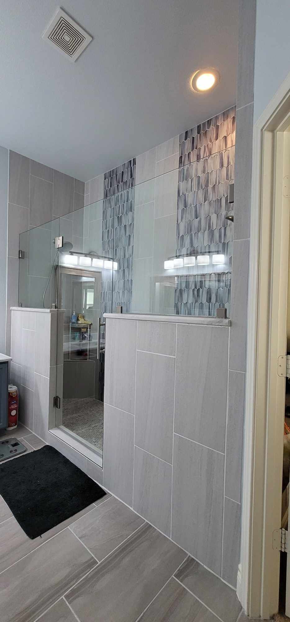 Bathroom with gray tiled walls, shower, and a black bath mat.