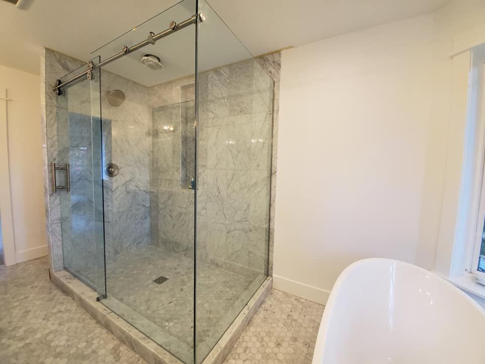 Bathroom with a glass shower enclosure and a white bathtub, marble tiling.