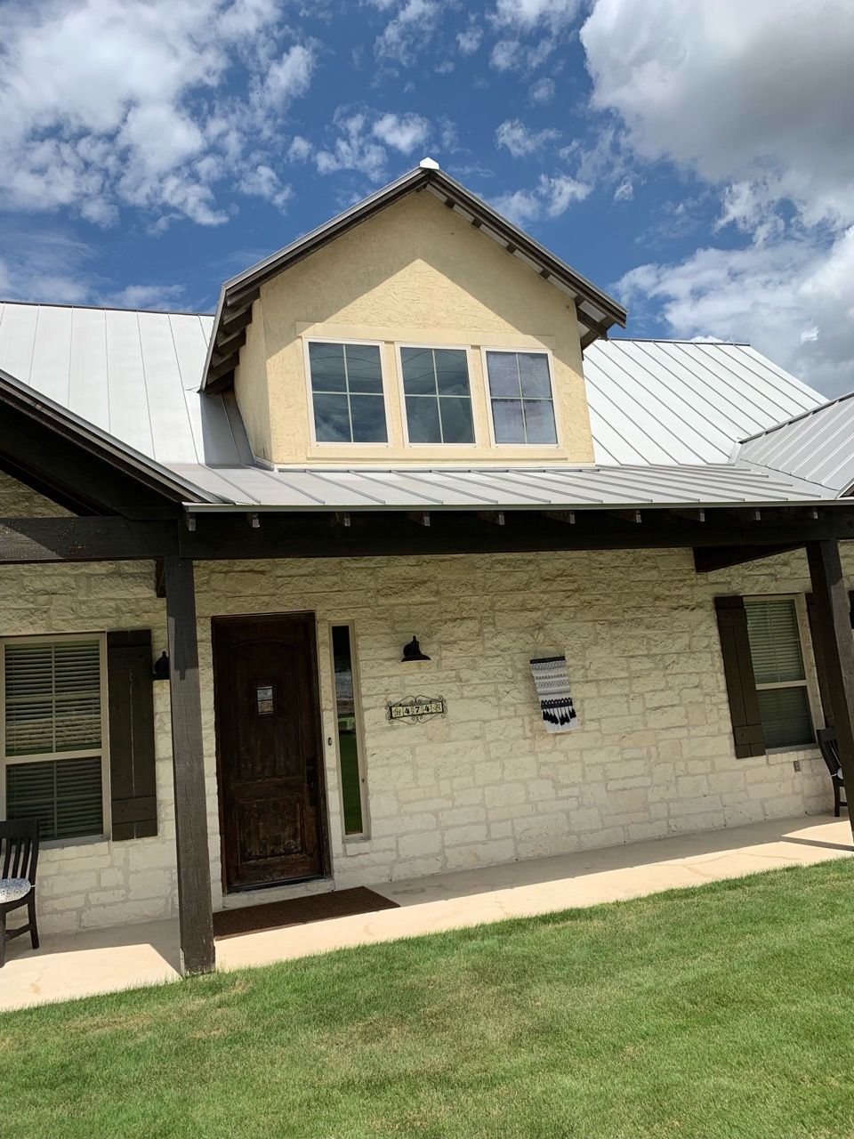 House exterior with light stone facade, metal roof, and covered porch under a partly cloudy sky.