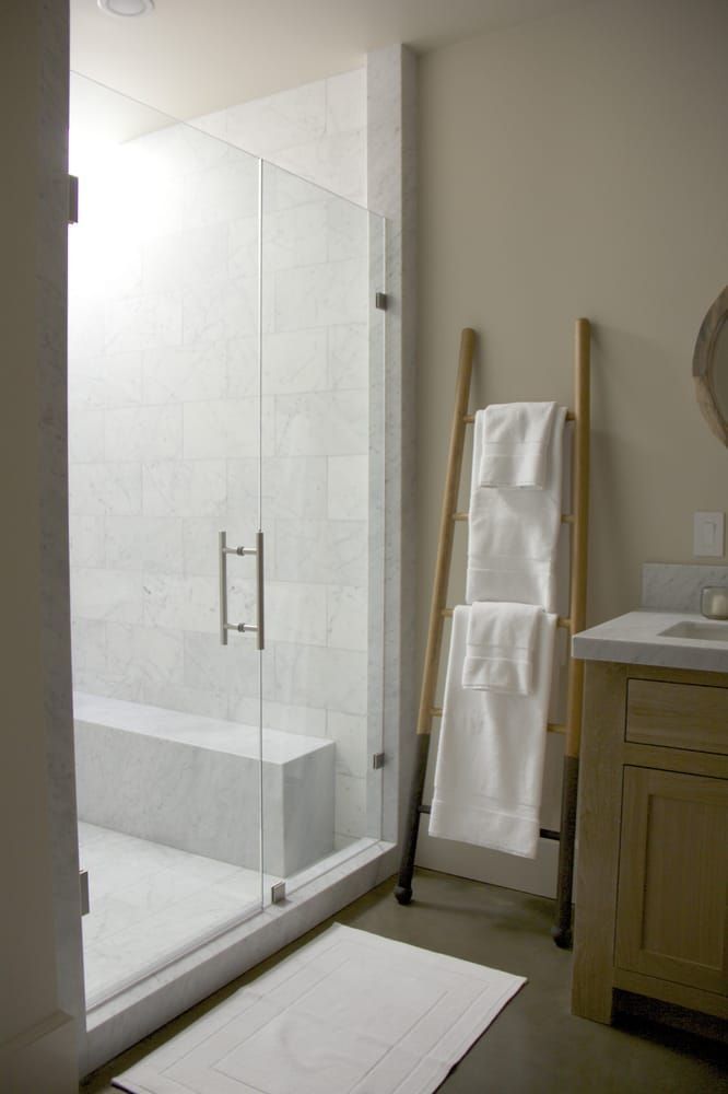 Modern bathroom with glass shower, towels on ladder, and wooden vanity.