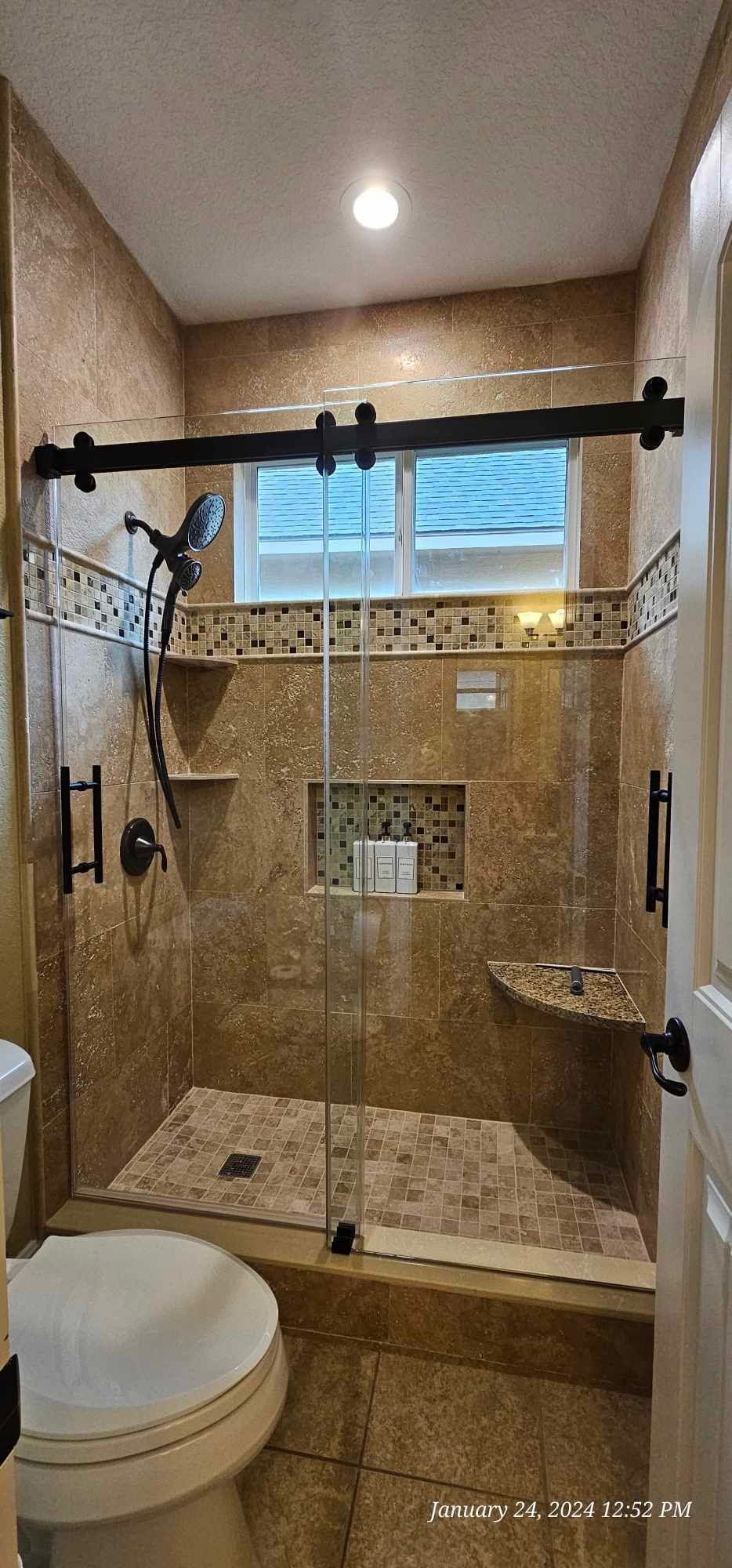 Bathroom with a stone tile shower, clear glass door, and black hardware. A toilet is visible.