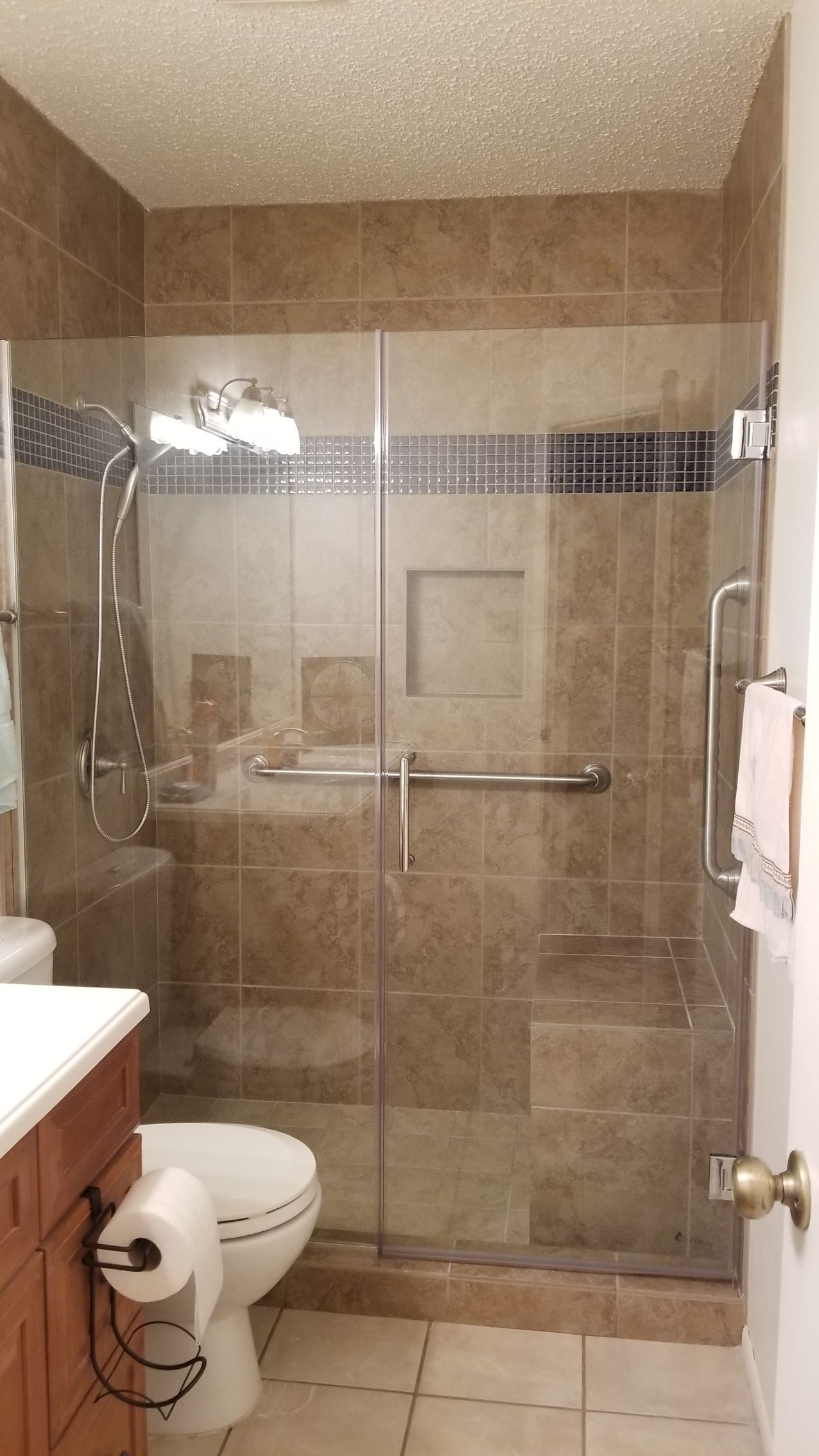 Bathroom with glass shower doors, brown tiled walls, toilet, and vanity.