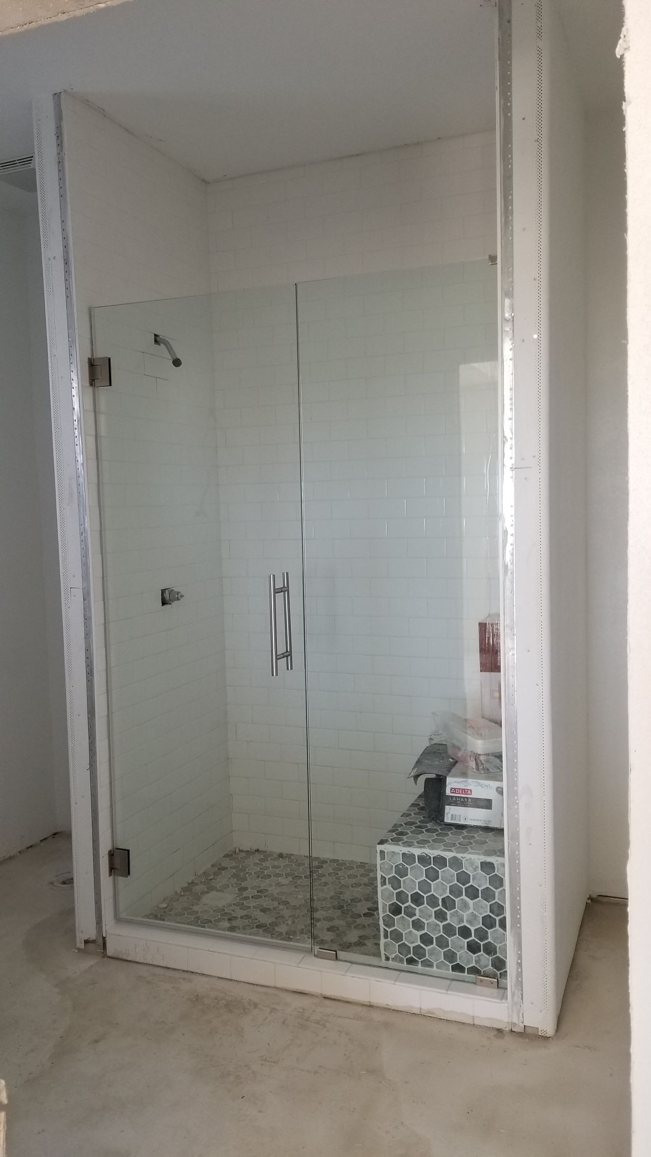 Glass shower enclosure with white tile walls and a mosaic tile floor.