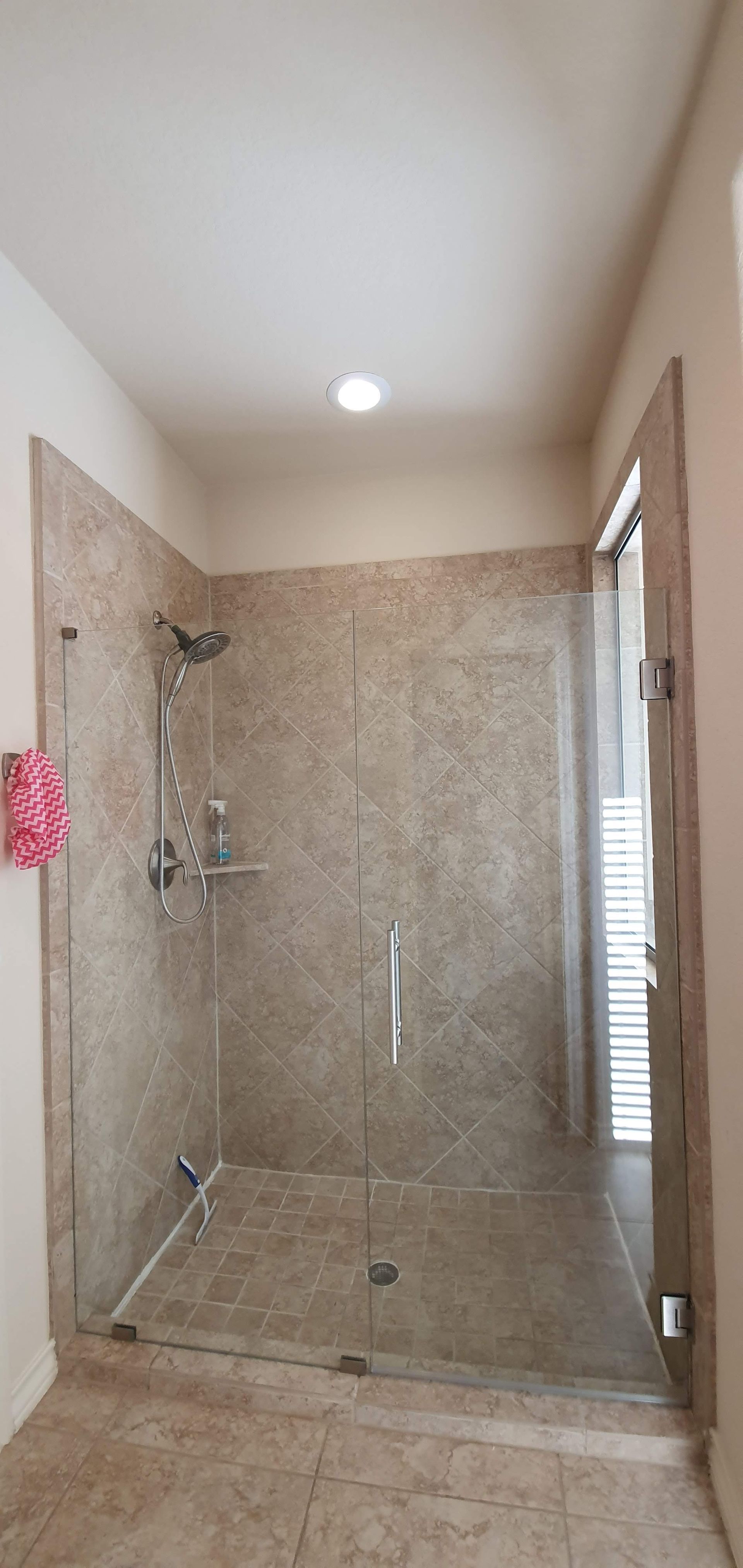 A shower with glass doors, tiled walls, and a silver shower head. The floor is tiled.
