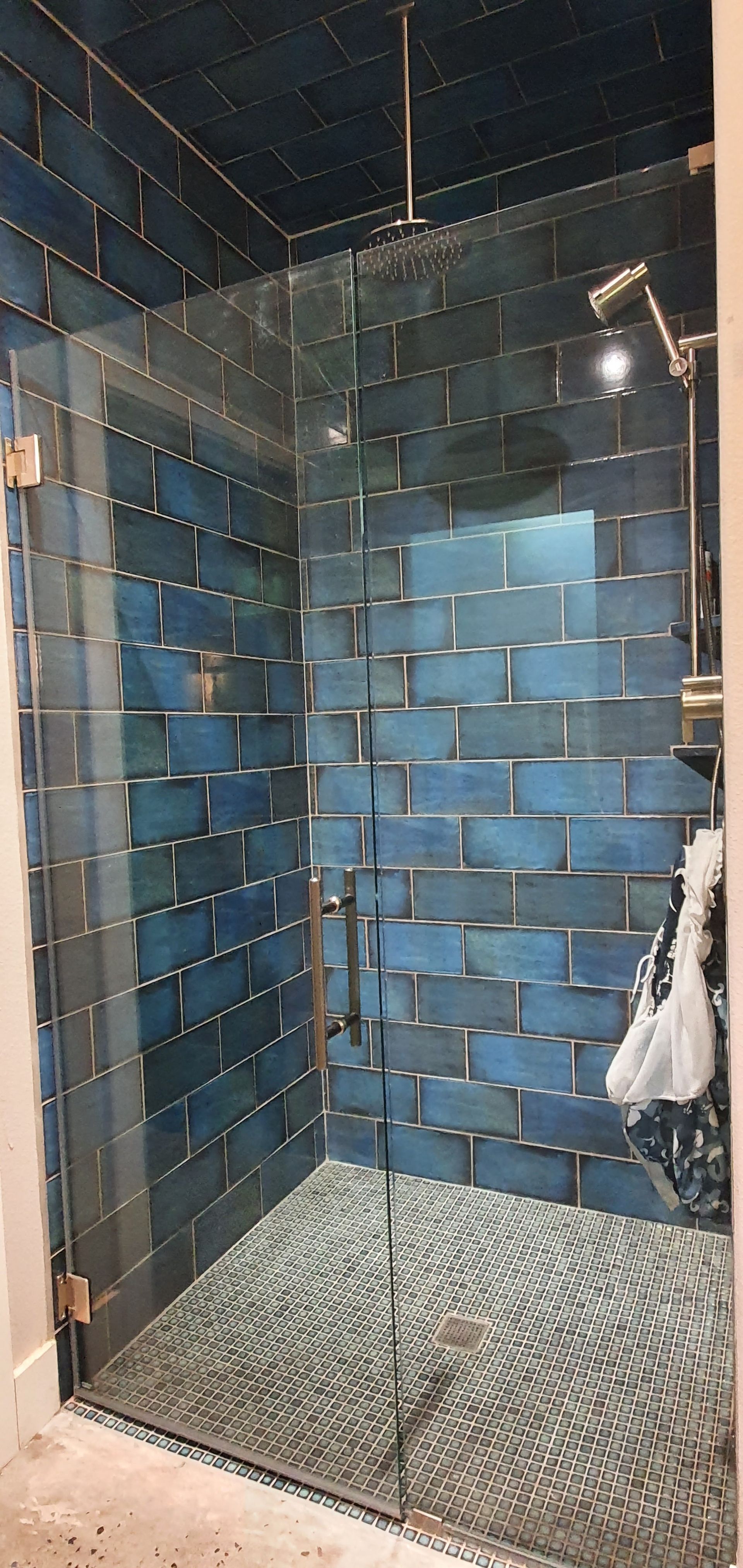 Shower stall with blue brick-like tiles, a pebble floor, and glass doors.