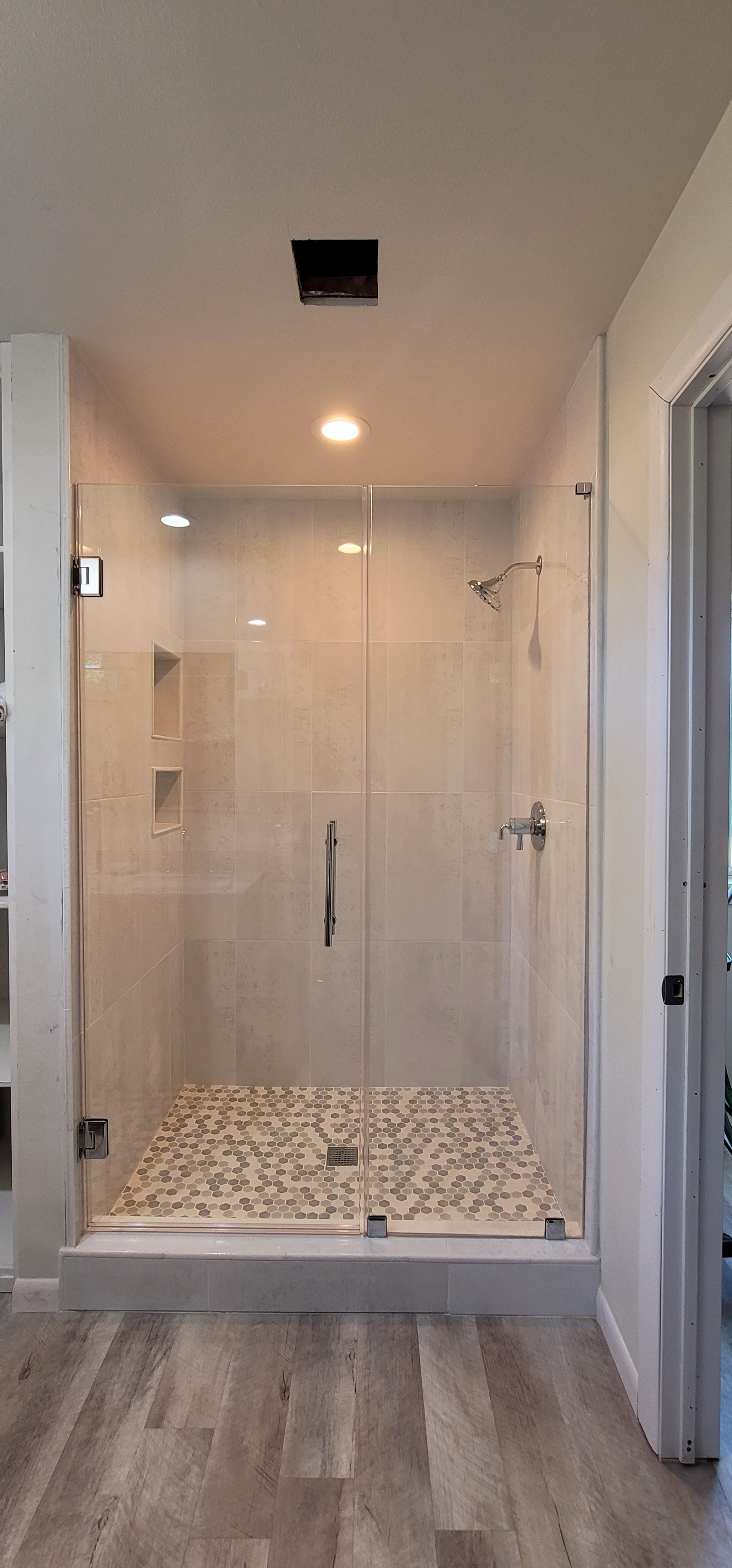 A walk-in shower with glass doors, pebble floor, and white tile walls.