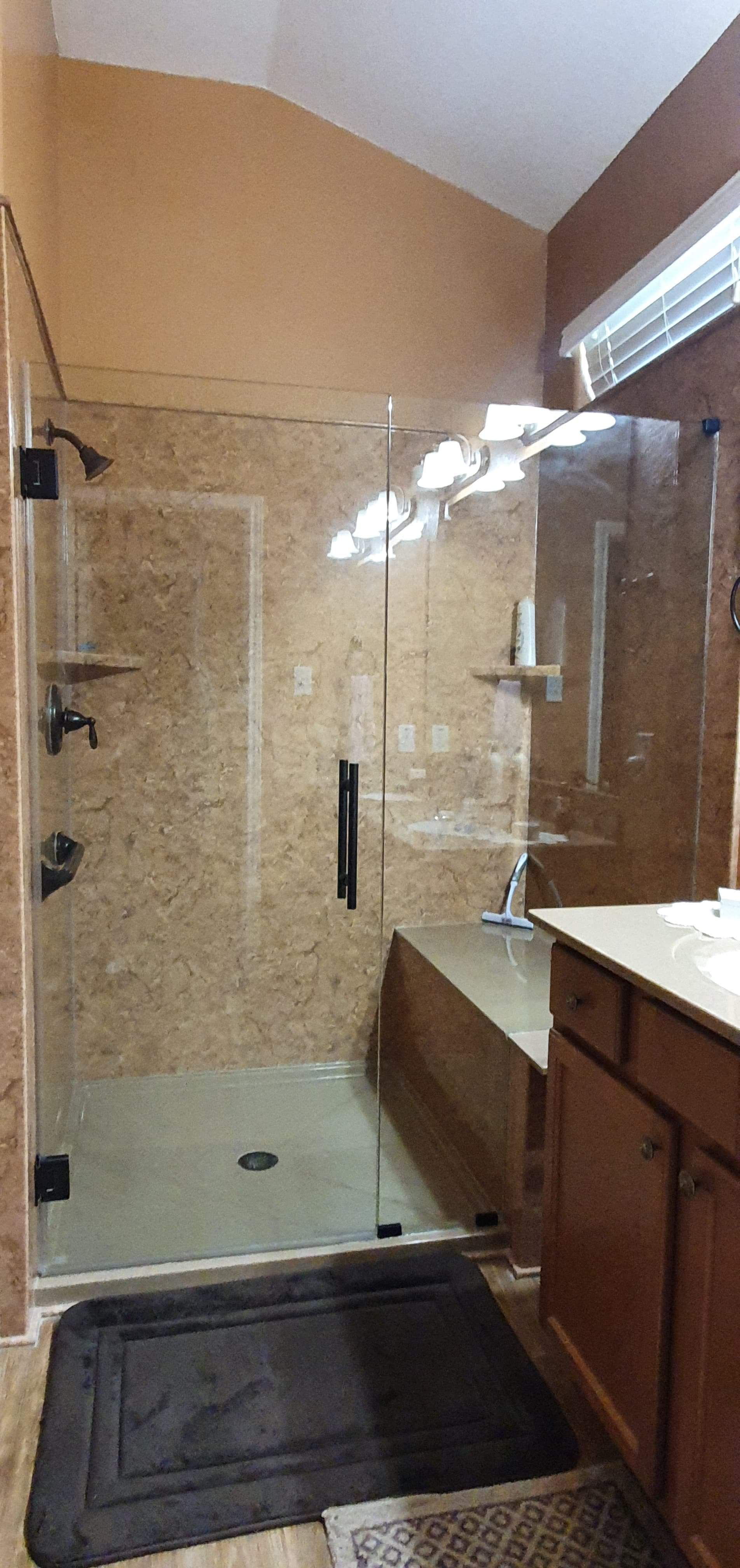 Bathroom with a glass shower, brown tile walls, and a dark rug on the floor.