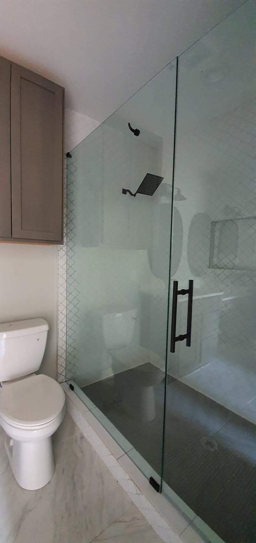 Bathroom with glass shower, toilet, and gray cabinets.