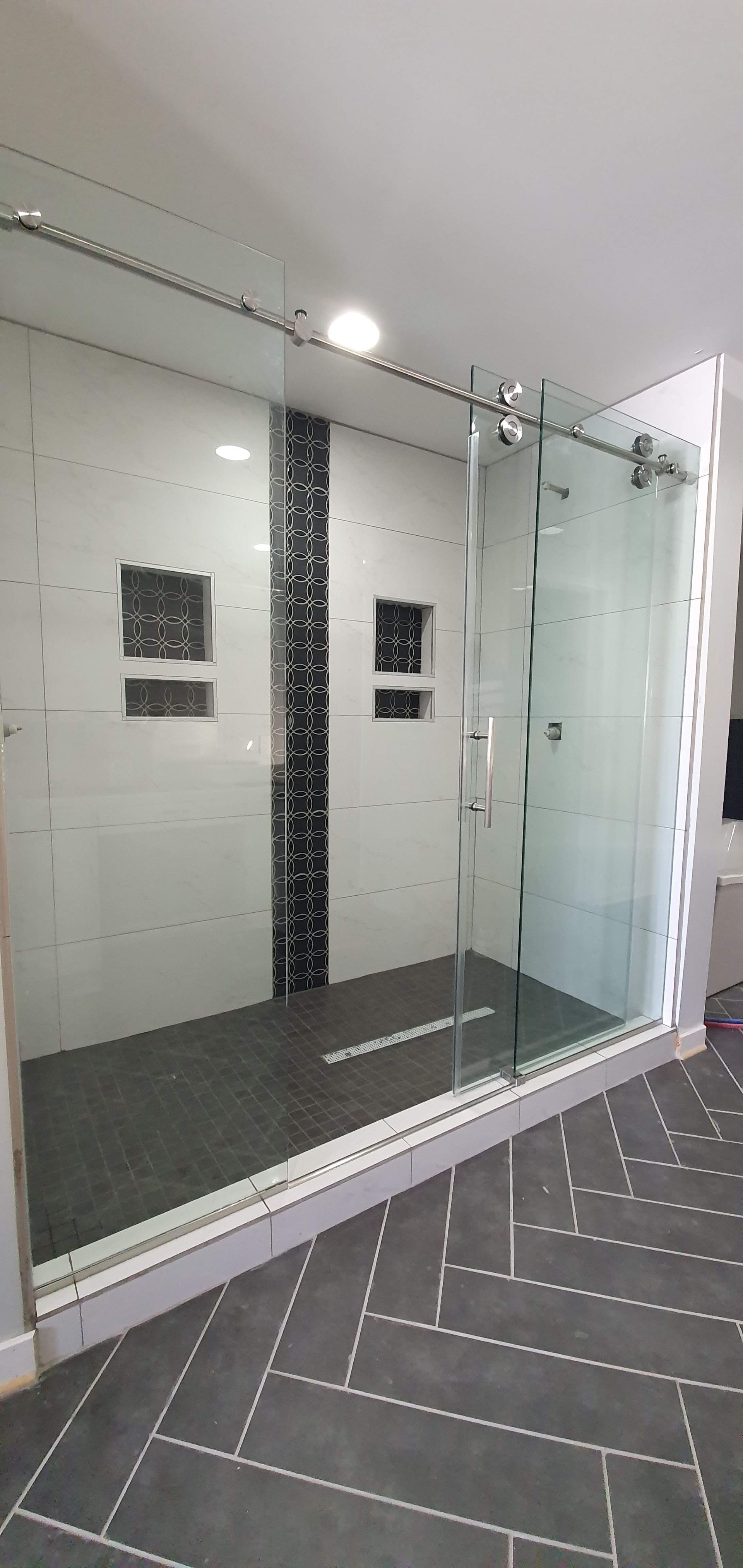 Modern walk-in shower with glass doors, white tiled walls, and dark gray herringbone floor.