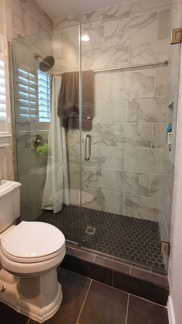 Bathroom with glass shower, marble tile, black pebble floor, and toilet.