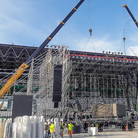 Stage scaffolding and cranes at an outdoor construction site with workers in high-visibility vests