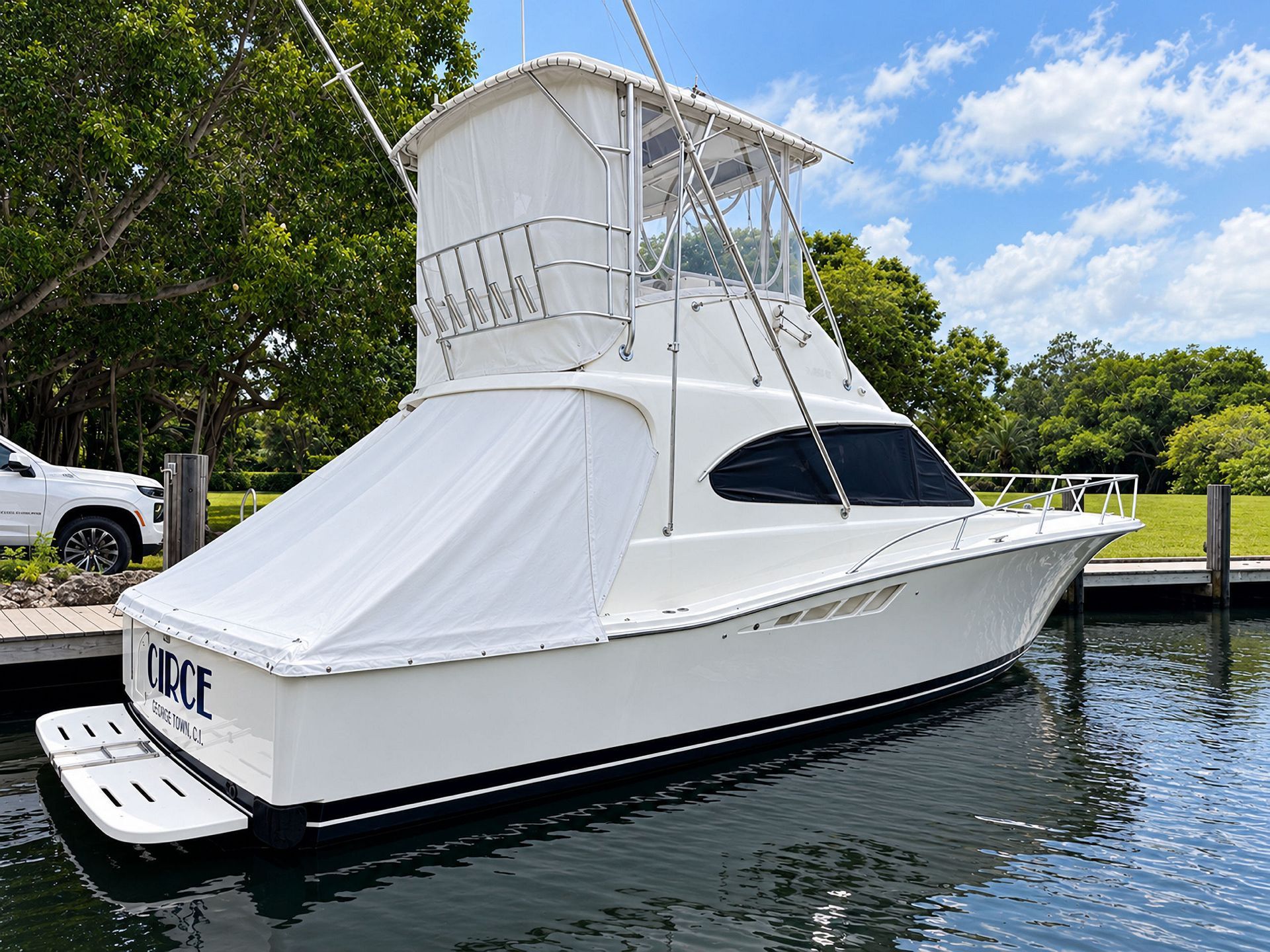 White yacht docked on calm water beside a wooded marina under a blue sky