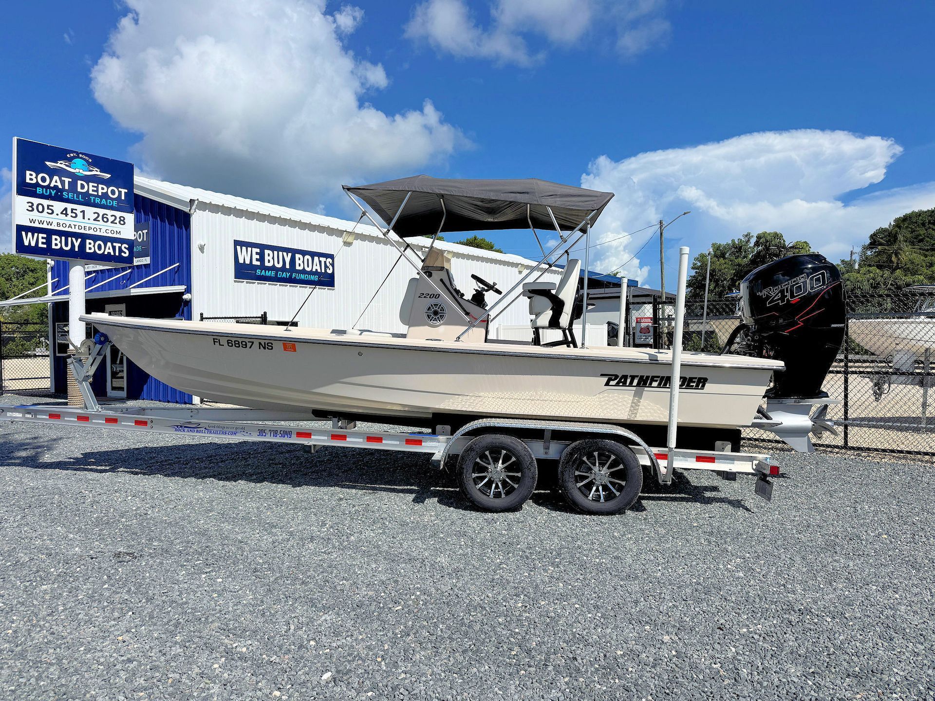 Tan center-console bay boat on a trailer at a boat lot under a blue sky