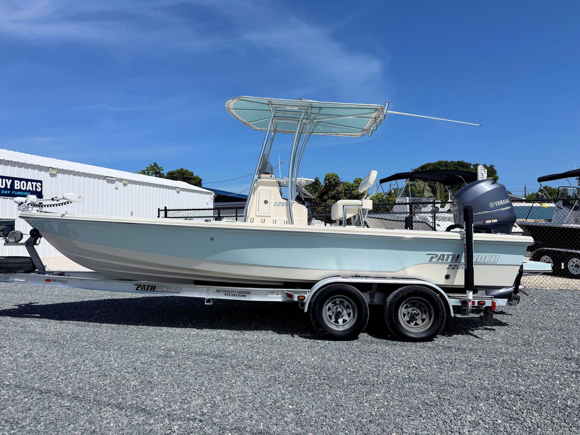 Center-console boat on a trailer in a gravel lot under a blue sky