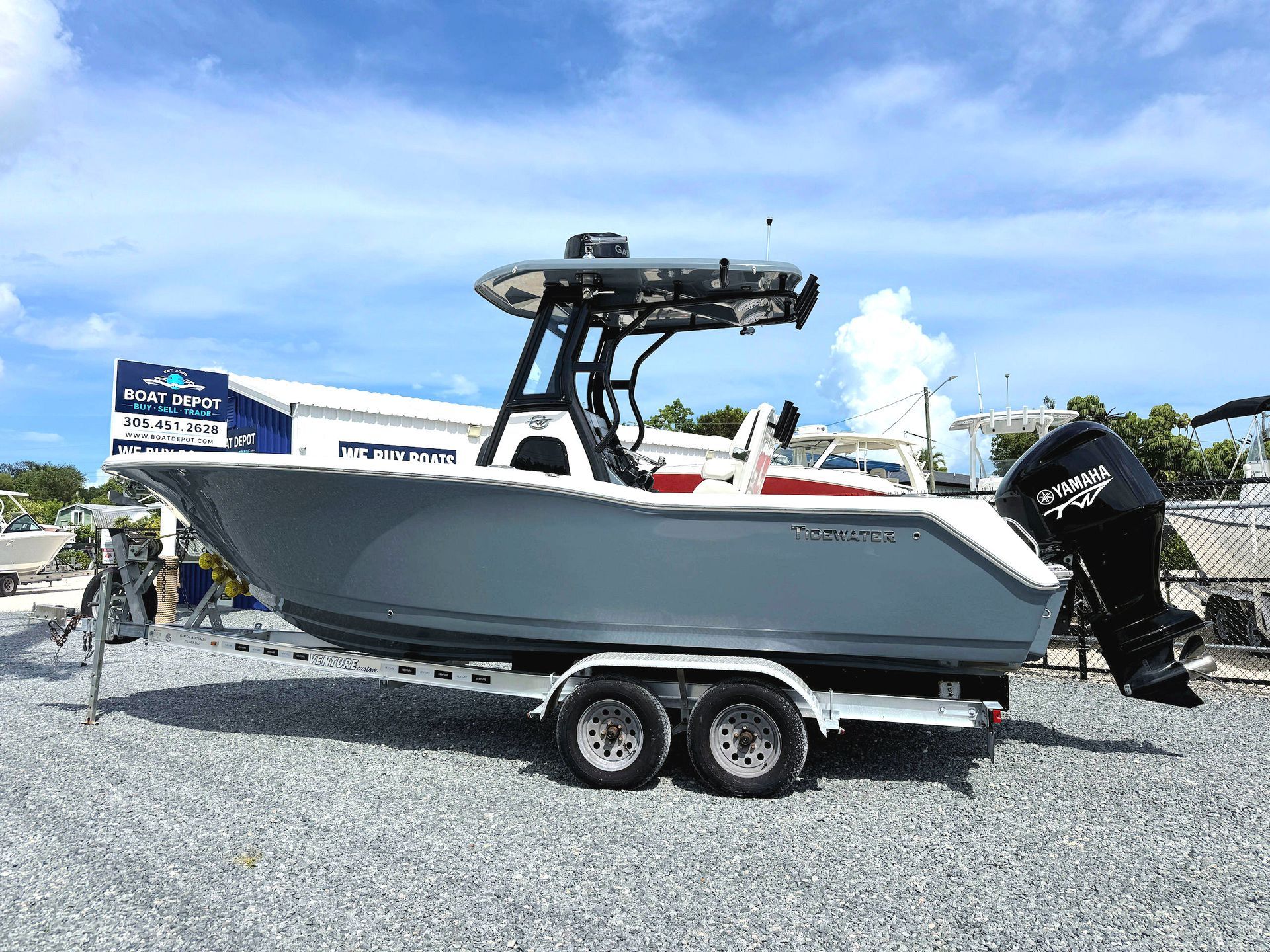 Gray center-console boat on a trailer with black outboard motor, parked on gravel under a blue sky.