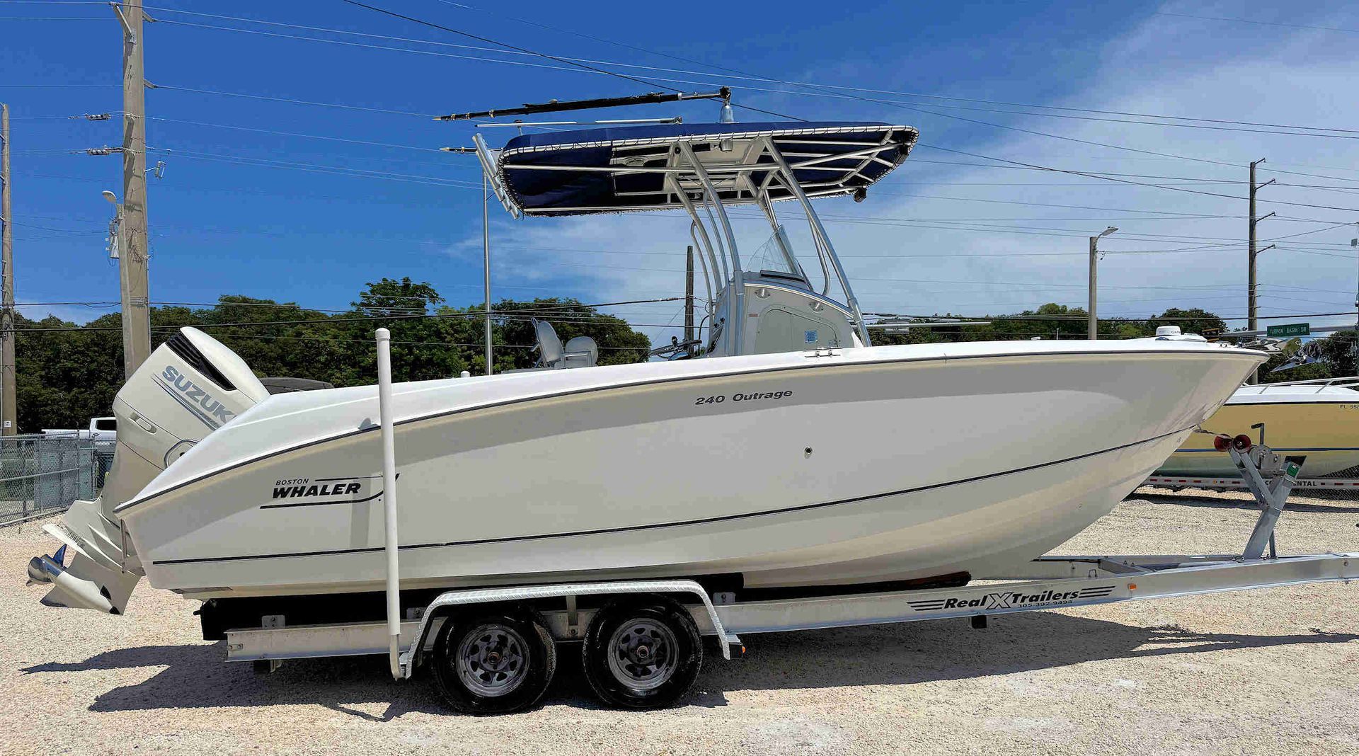 White center-console boat on a trailer parked outdoors under a blue sky.